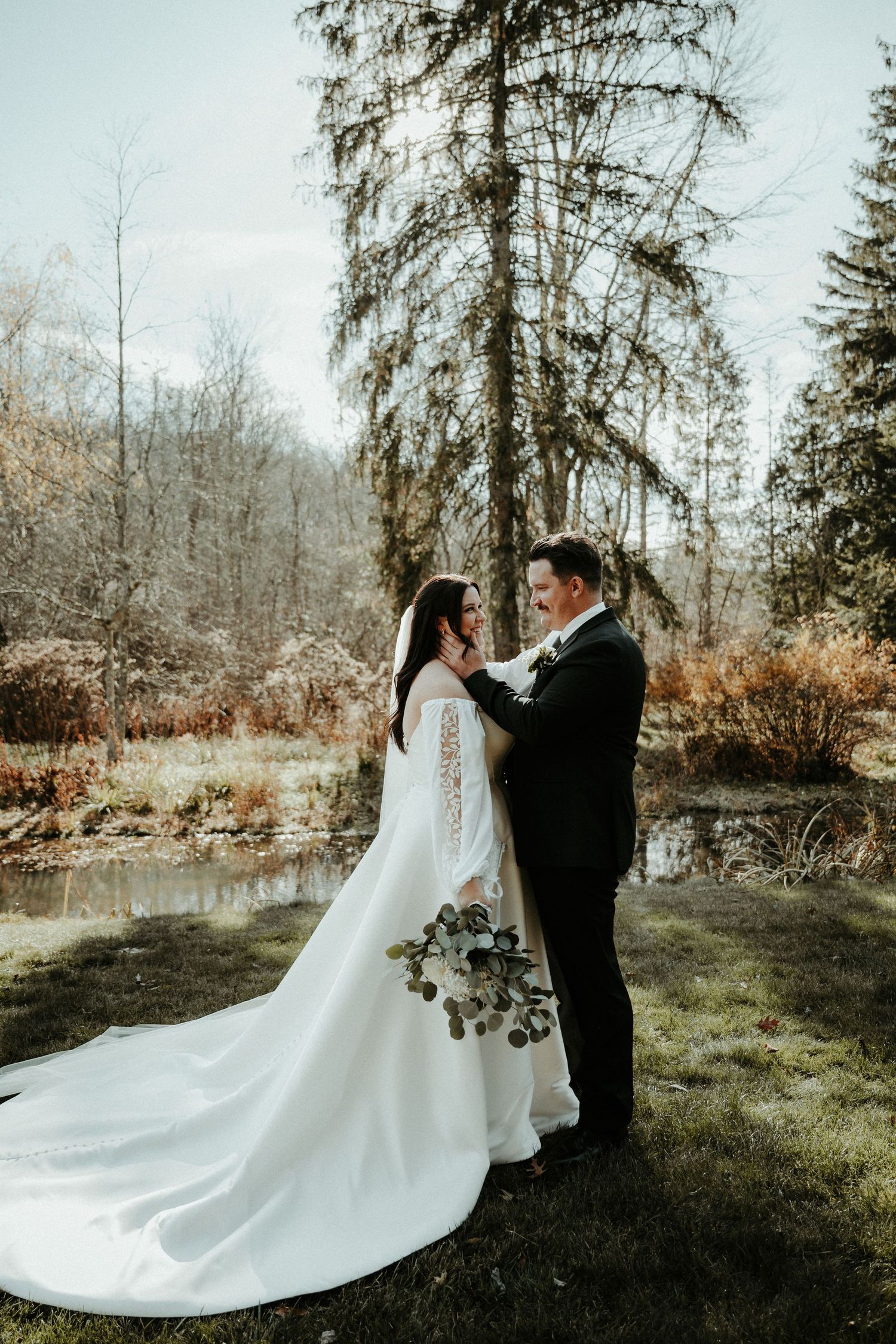 A romantic wedding portrait in front of tall trees and a pond with a long flowing white dress. Pittsburgh Wedding Photographer