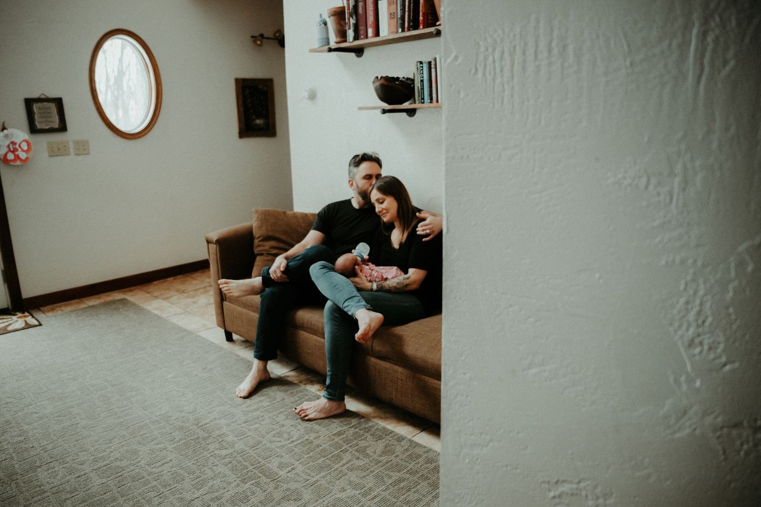 A person sits casually on a brown leather couch in a minimalist room with white walls and a circular mirror.