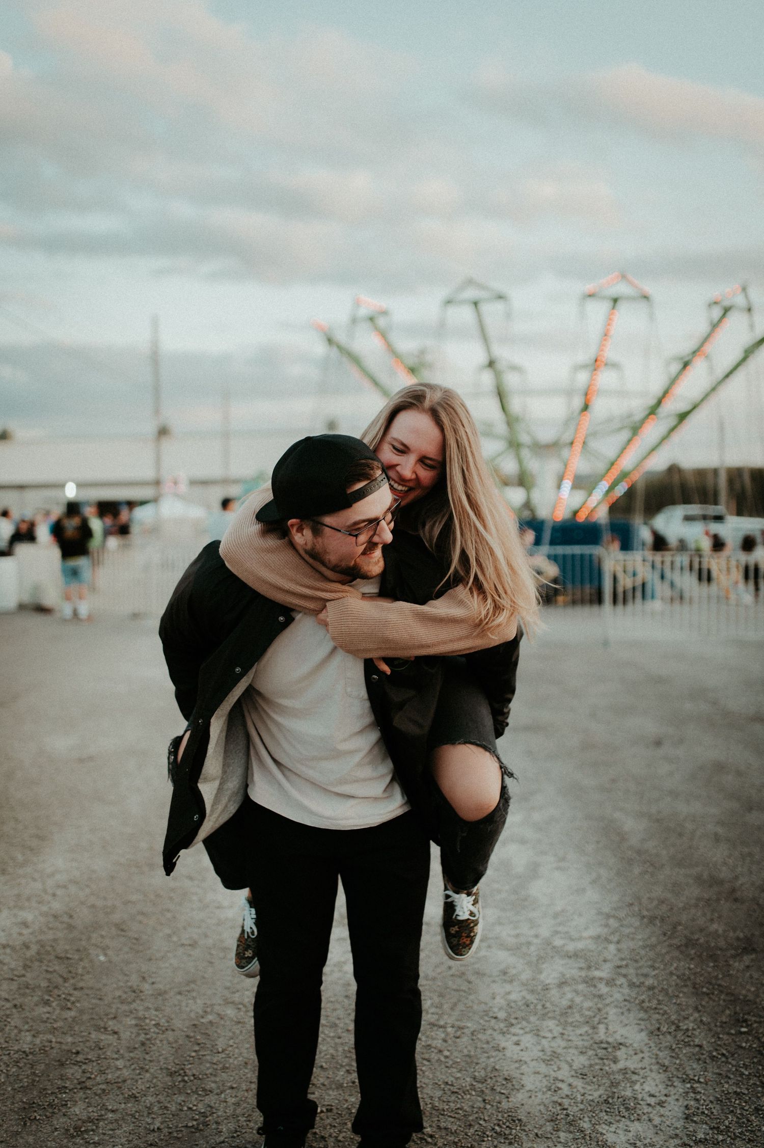 Playful piggyback ride at carnival with colorful rides in background. Pittsburgh Wedding Photographer