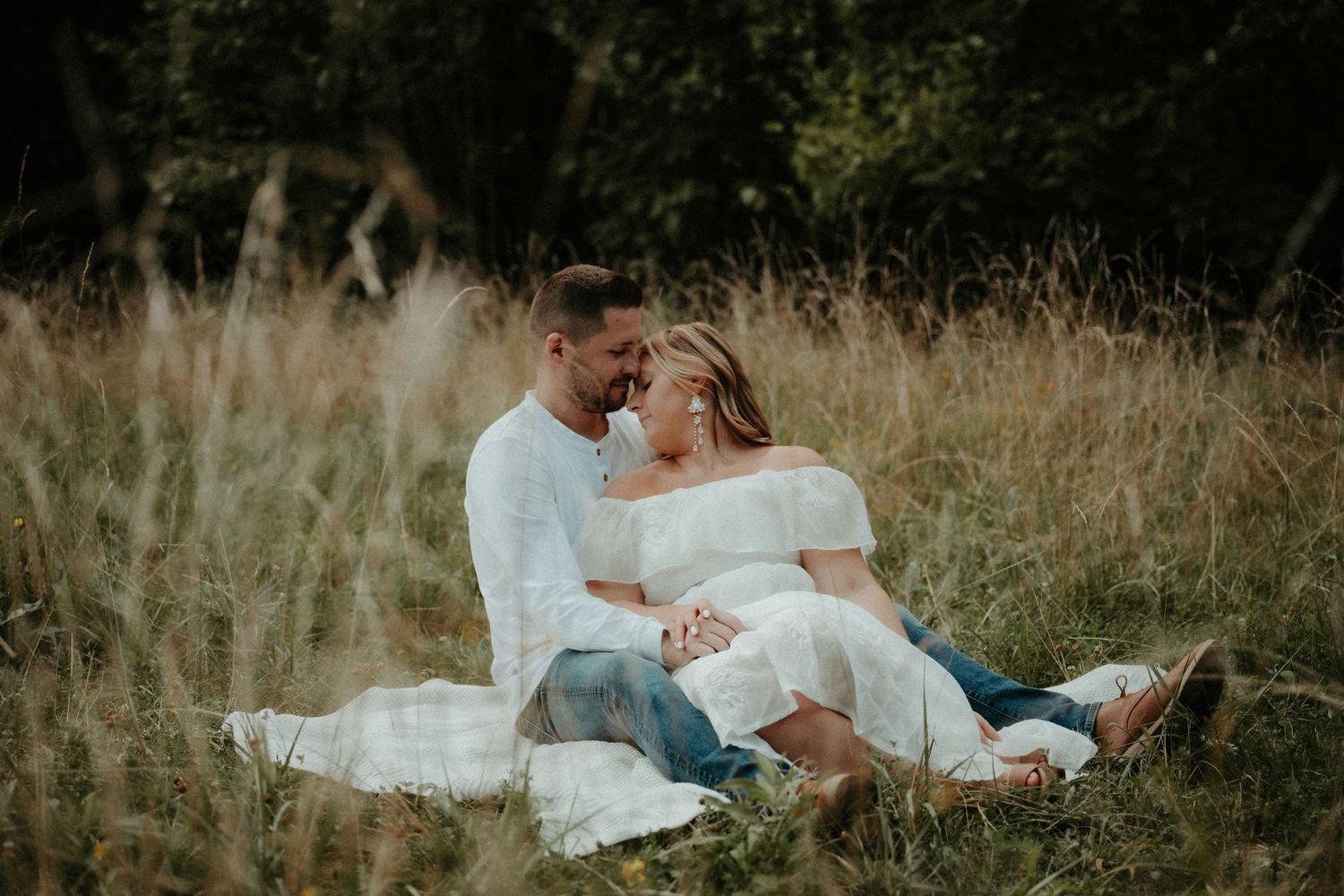 A couple in light clothing sits intimately in a grassy meadow during golden hour. Pittsburgh Wedding Photographer