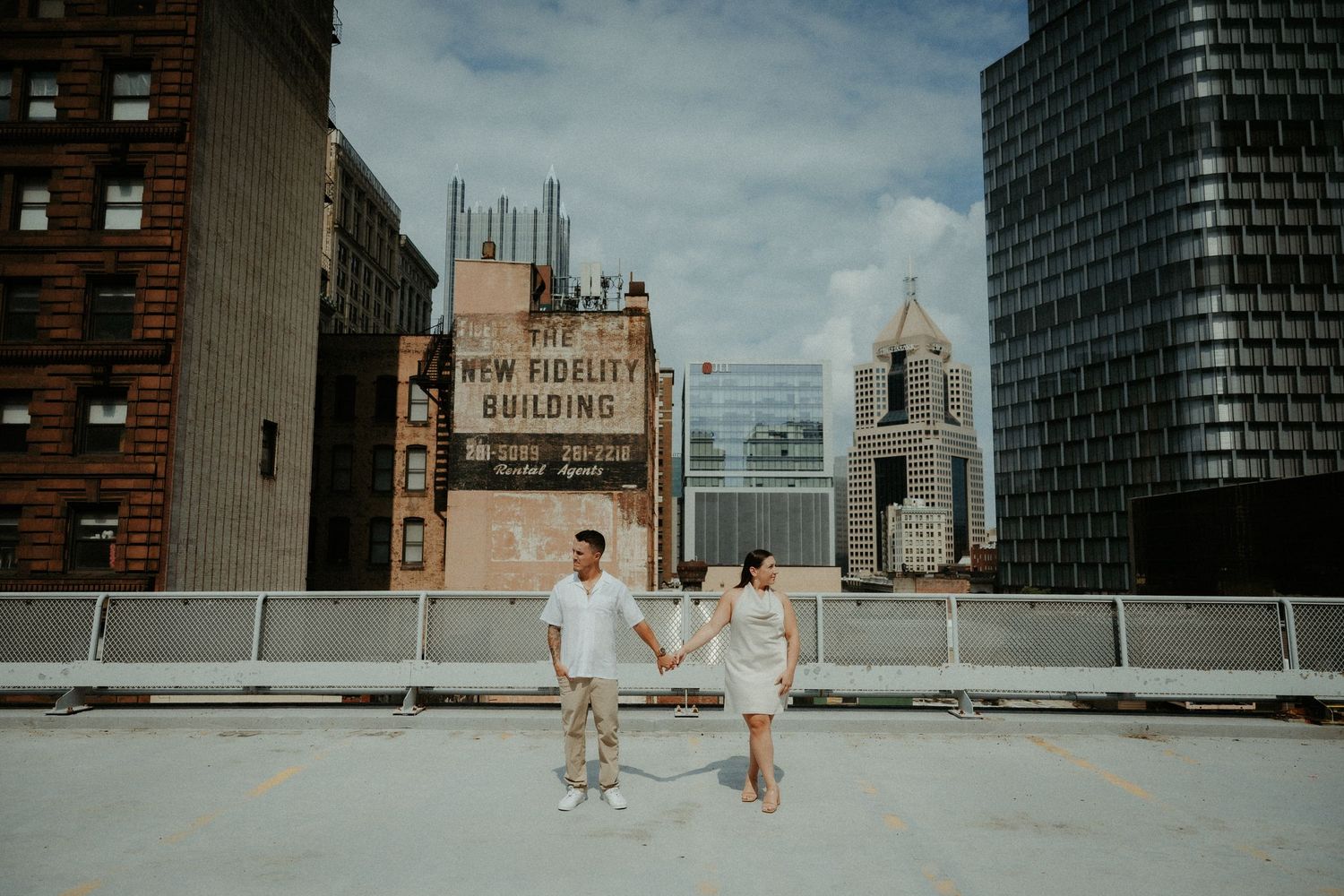 Two people in formal attire walk along a rooftop terrace with city buildings in the background at sunset. Pittsburgh Wedding Photographer