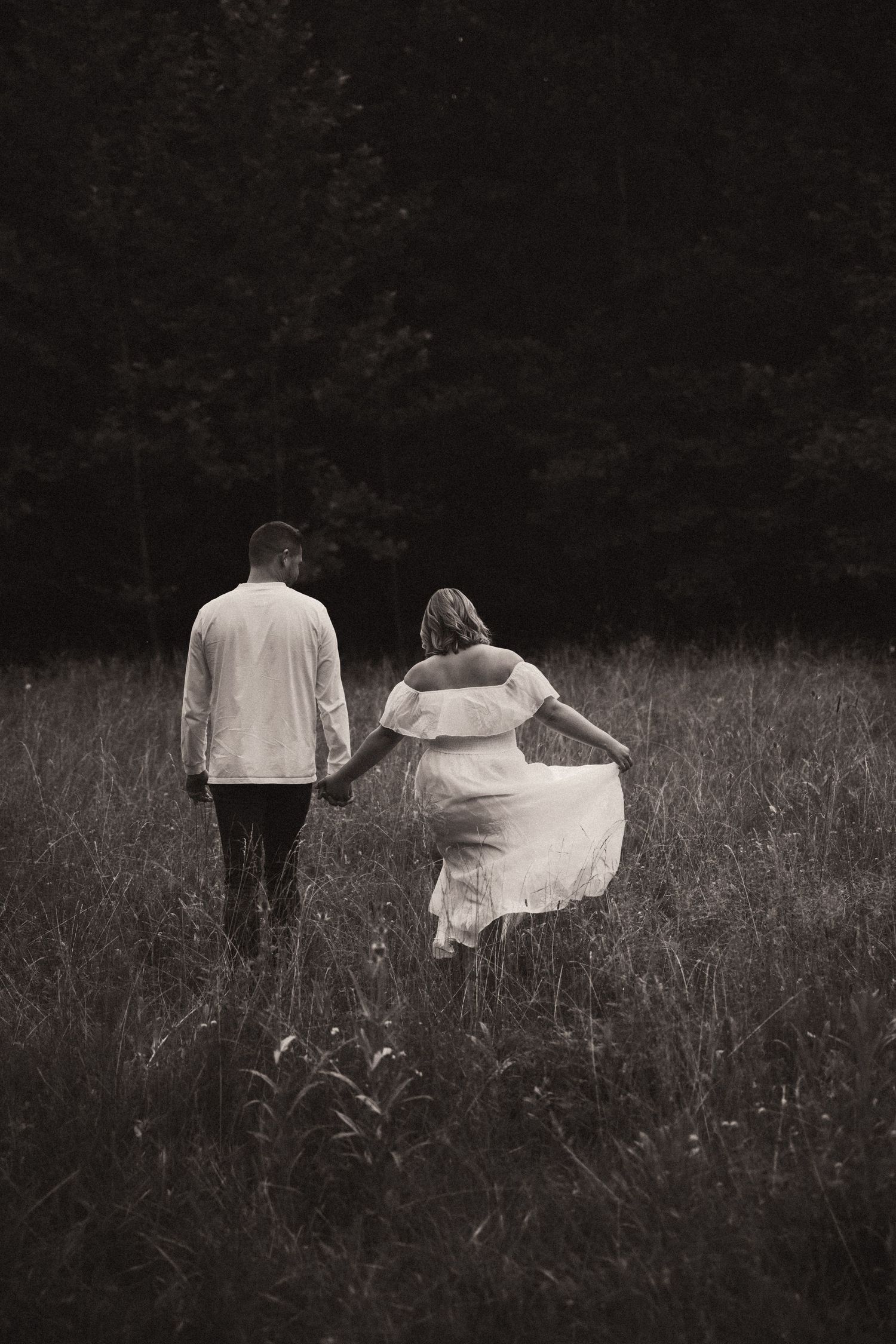 A couple walks hand in hand through a meadow in black and white, creating a romantic and dreamy atmosphere. Pittsburgh Wedding Photographer