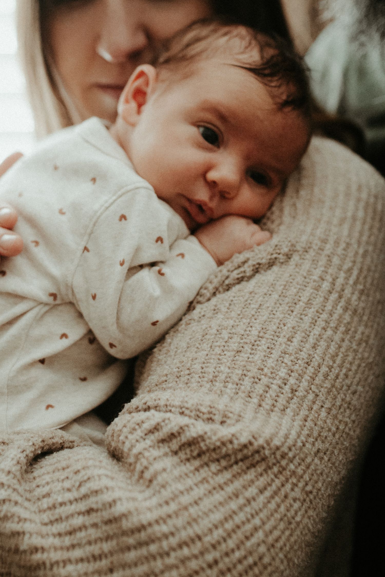 Sweet newborn baby in polka dot sleeper rests against soft knit sweater.