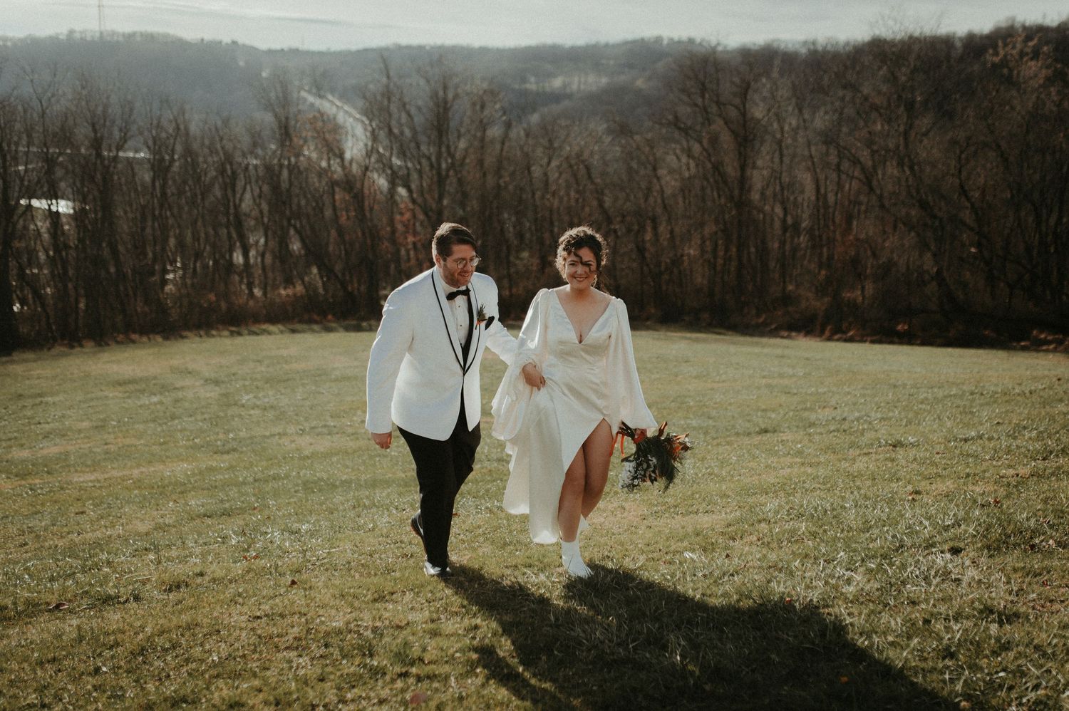 A couple runs joyfully through a hillside meadow, with the bride's white dress flowing in the wind. Pittsburgh Wedding Photographer