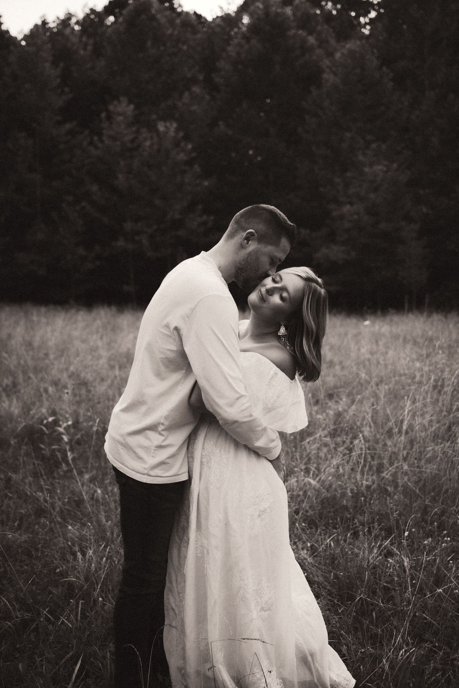 A romantic black and white photo of a couple embracing in a meadow with trees in the background. Pittsburgh Wedding Photographer