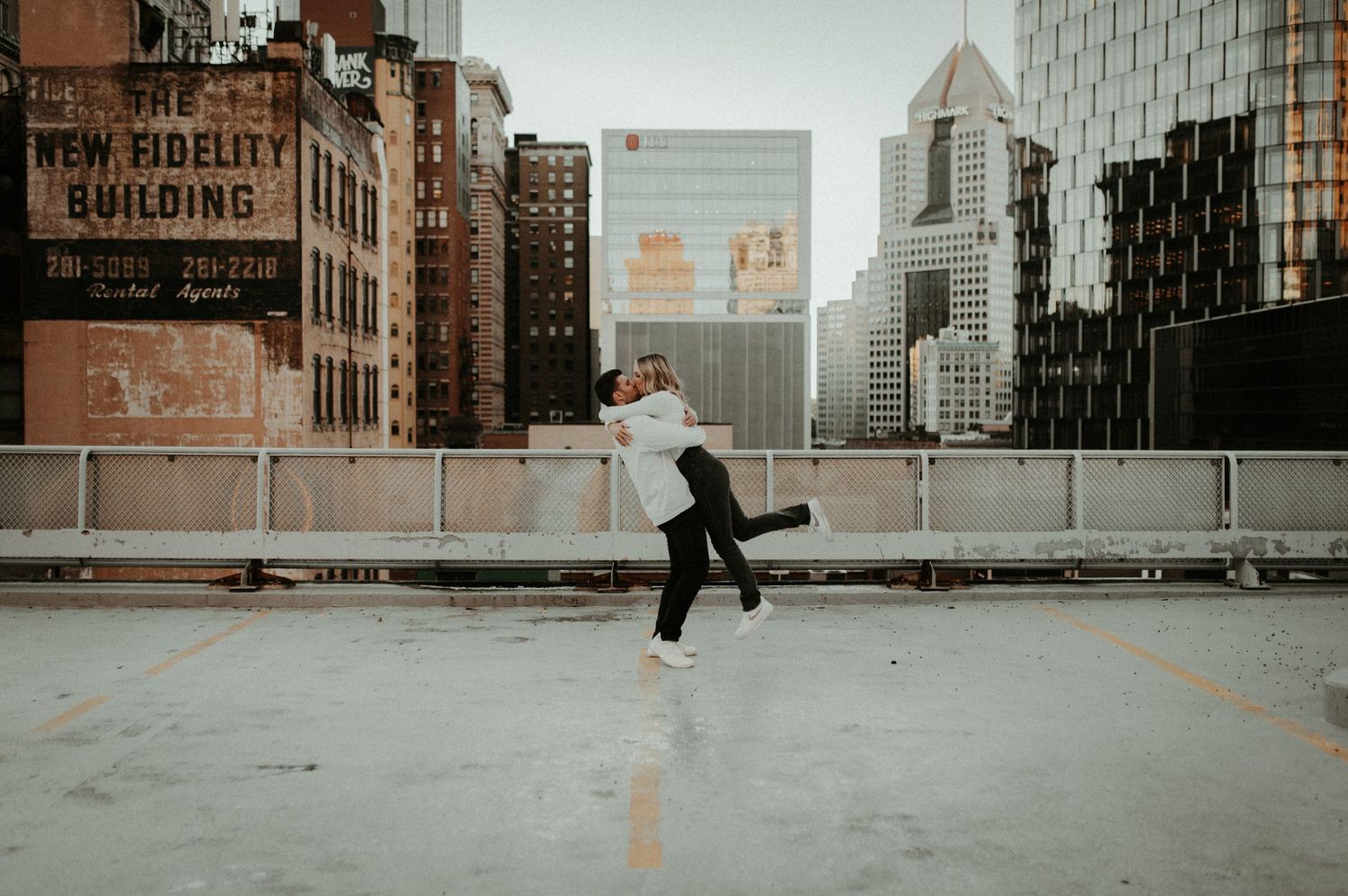 A person leaps joyfully on an urban rooftop with city skyline in background. Pittsburgh Wedding Photographer