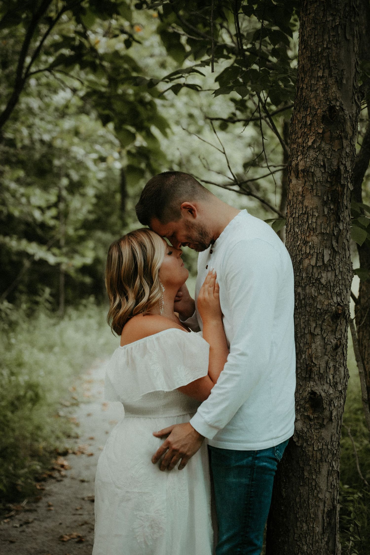 A romantic couple shares tender moments together on a woodland path surrounded by lush green trees. Pittsburgh Wedding Photographer