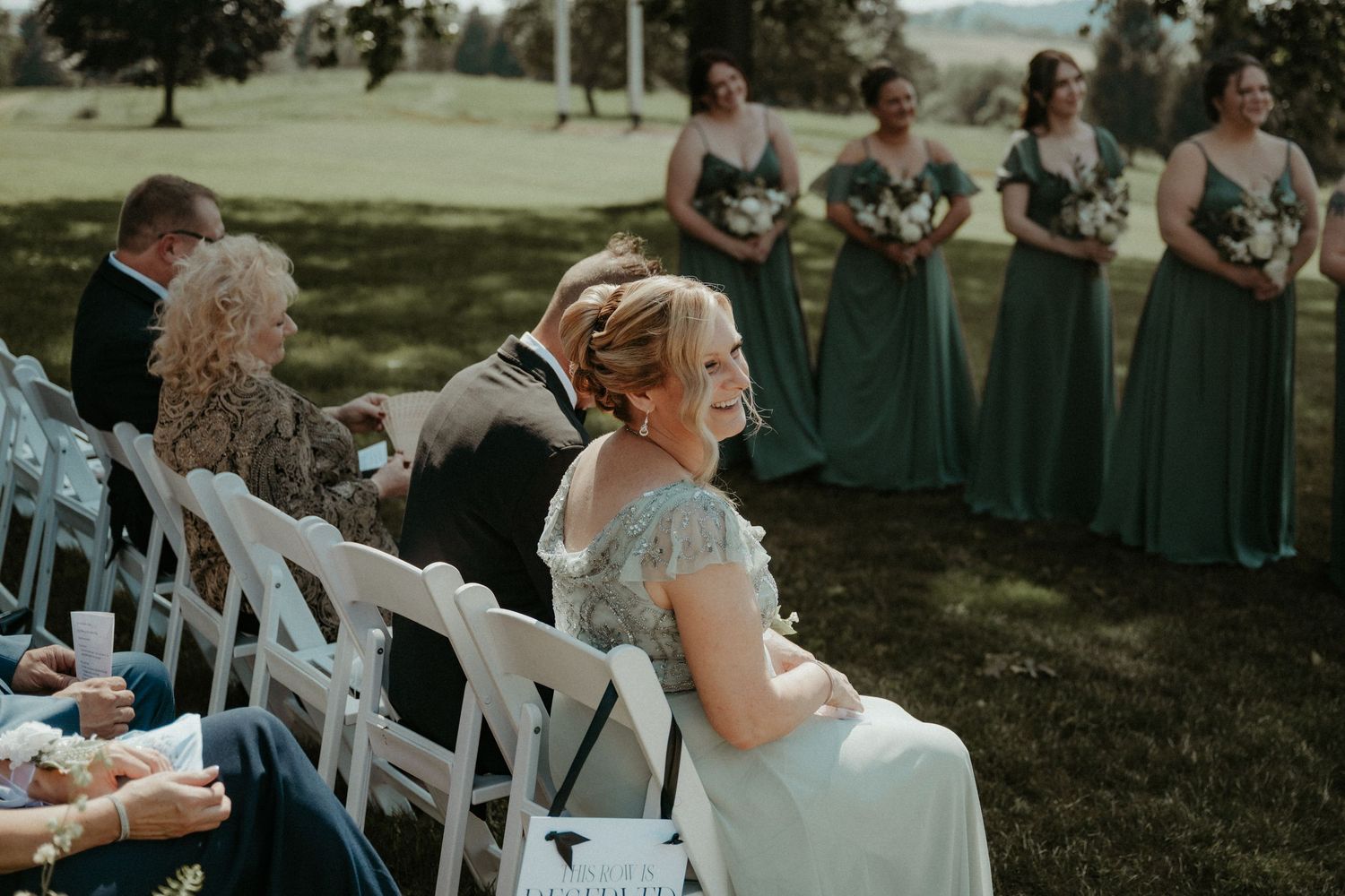Outdoor wedding ceremony seating area with white chairs arranged in rows on a grassy lawn under shade trees.