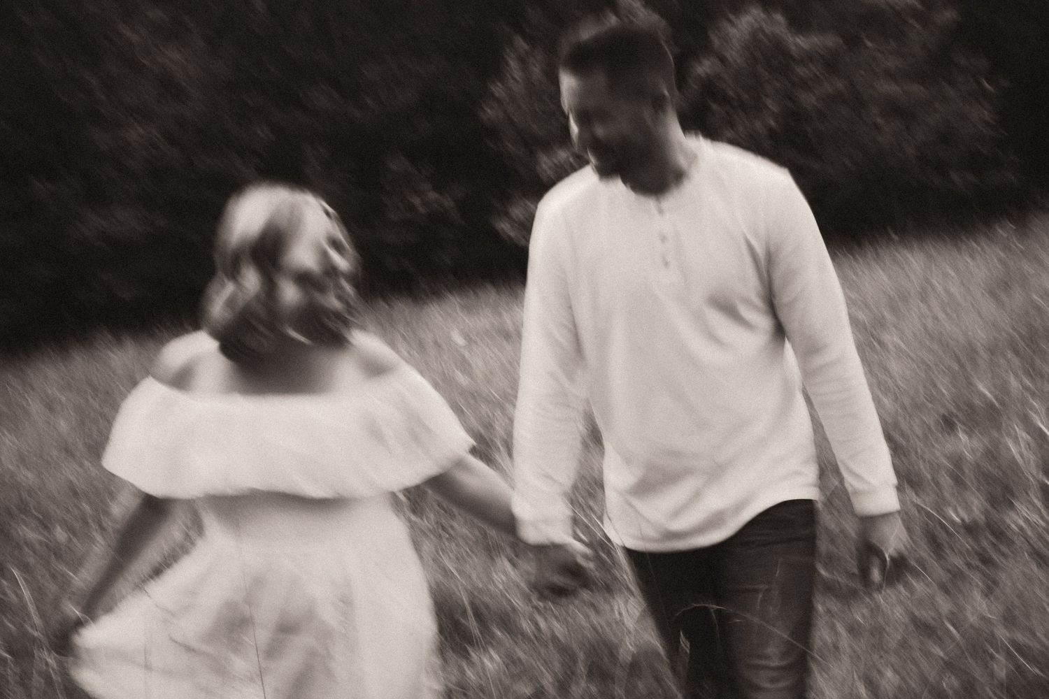 A black and white photograph shows two people walking together in a grassy field on a summer day.