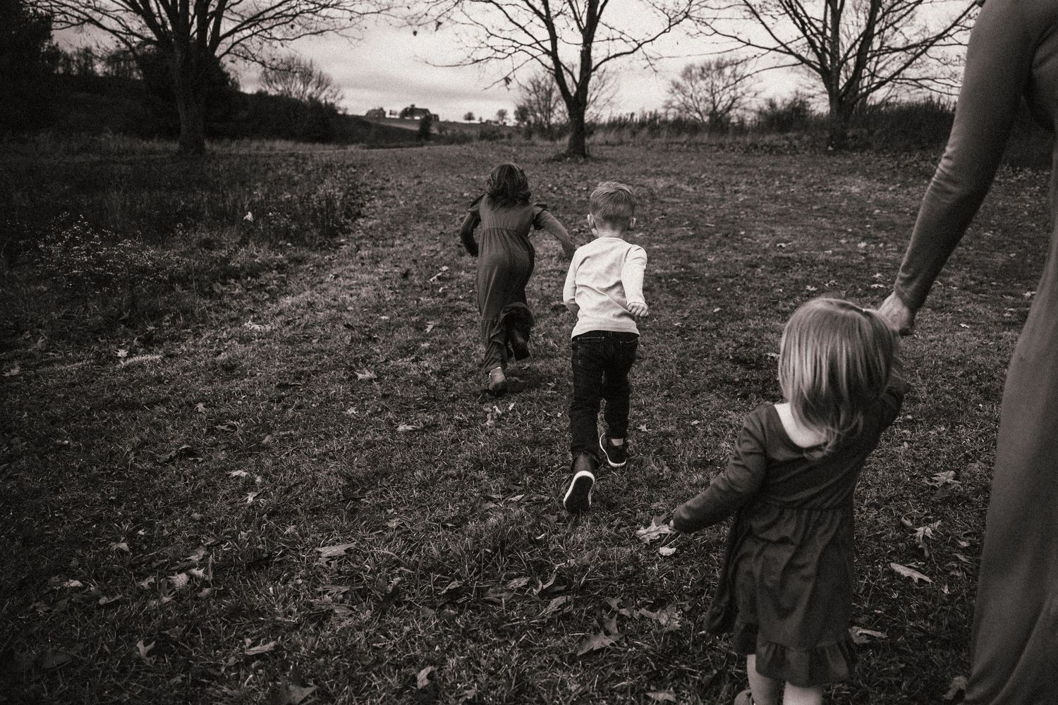 Children running through a field on a cloudy day captured in black and white.