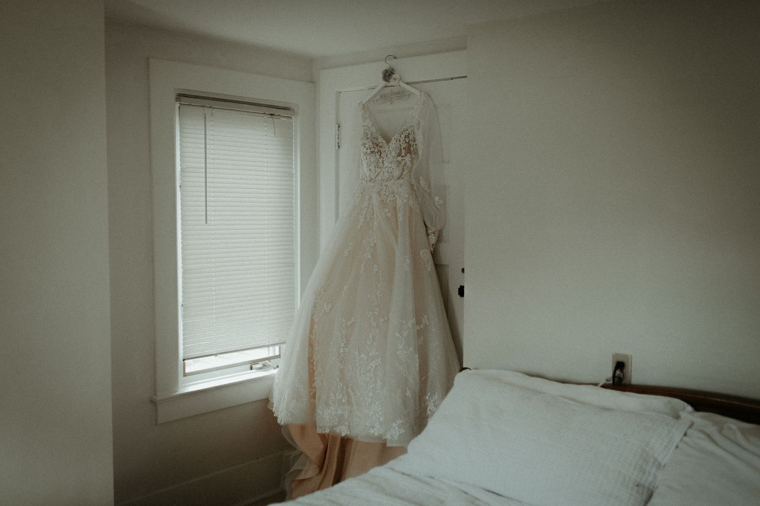 Elegant lace wedding dress hanging in bedroom window with soft natural light. Pittsburgh Wedding Photographer