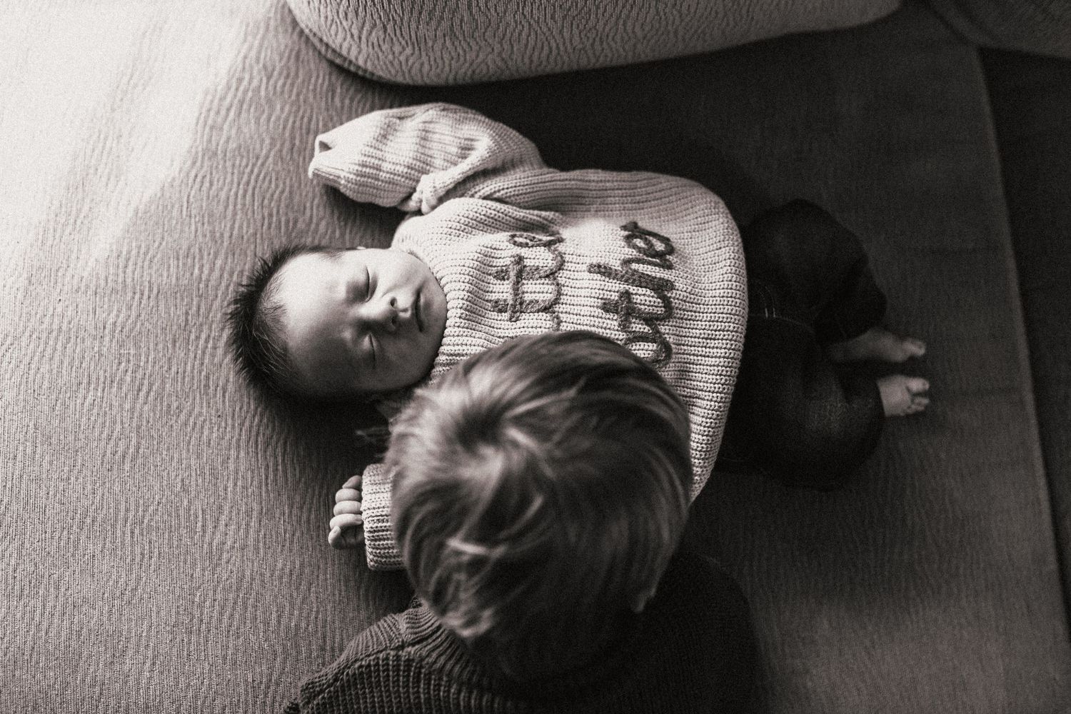 Two young siblings sharing a quiet moment together on a gray couch.