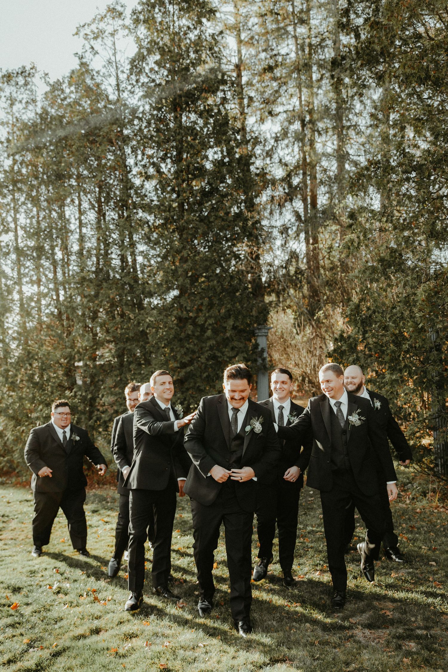 Wedding party of groomsmen in black suits posing outdoors among tall trees. Pittsburgh Wedding Photographer