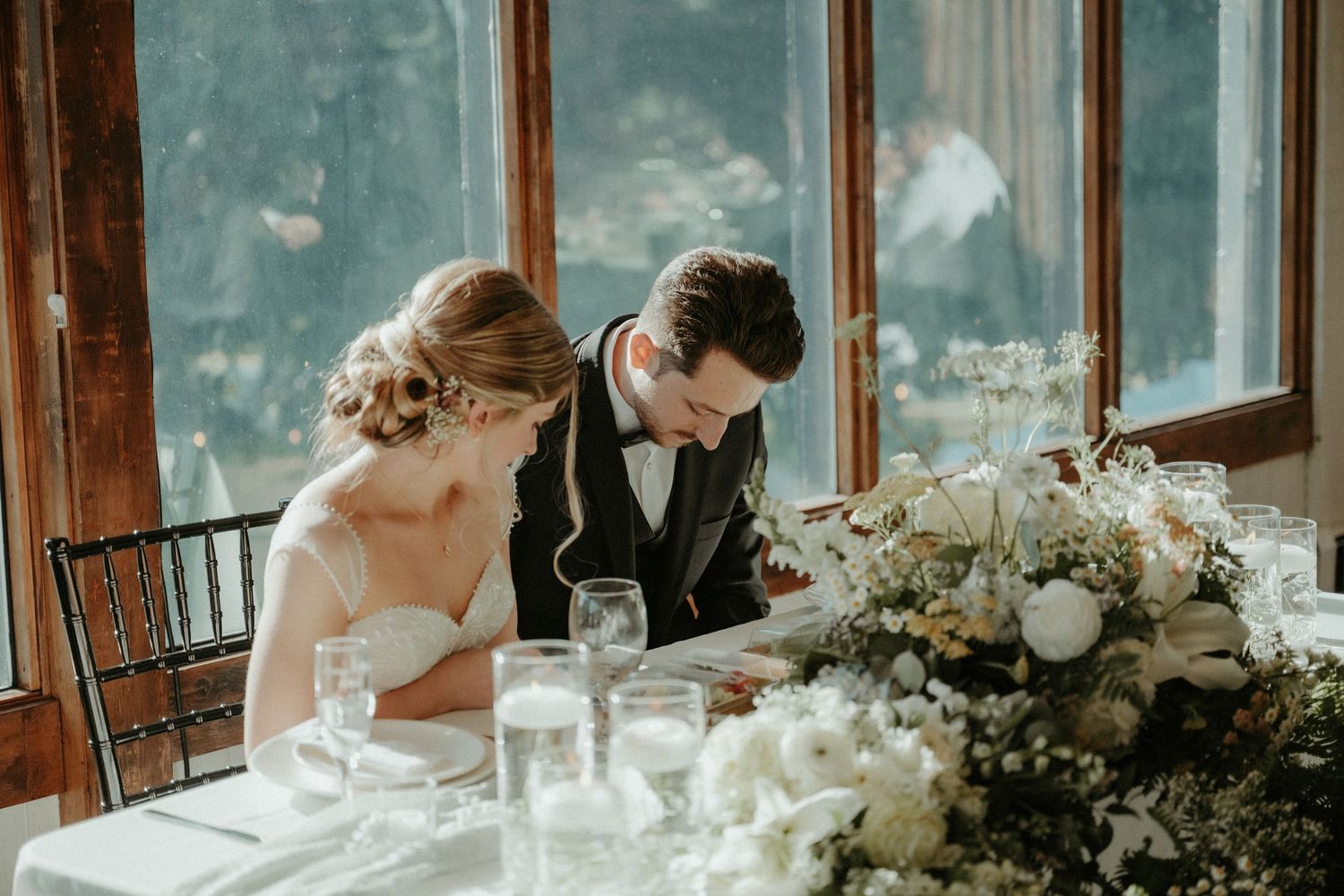 A couple in wedding attire sits at an elegantly decorated table with white floral arrangements. Pittsburgh Wedding Photographer