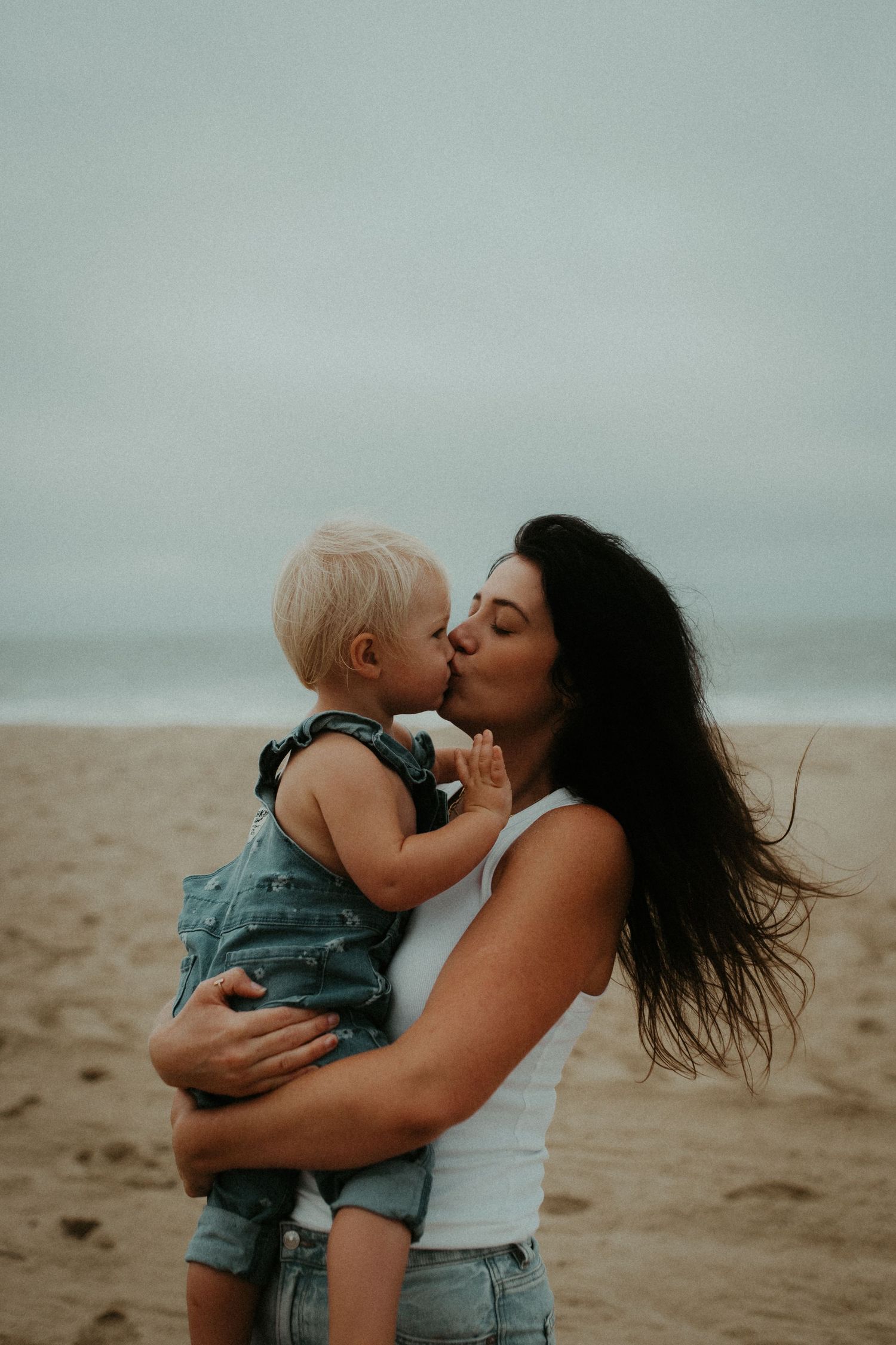 A tender moment between parent and toddler sharing a kiss on a misty beach.
