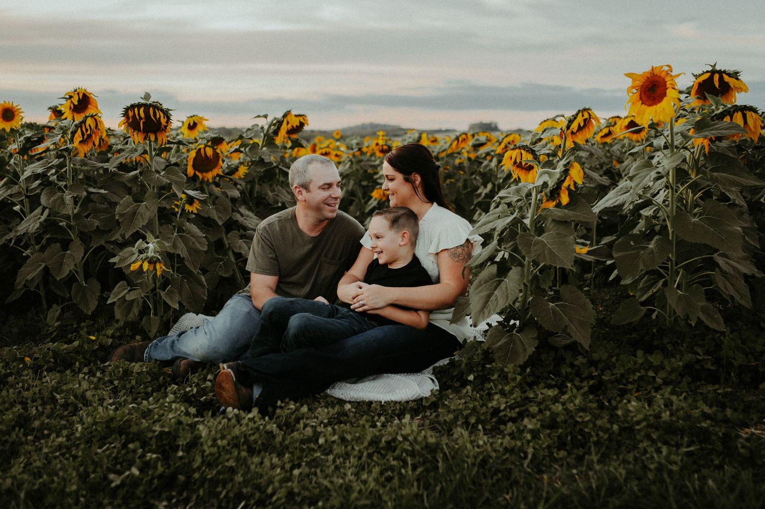 Family relaxing together in a beautiful sunflower field during golden hour.