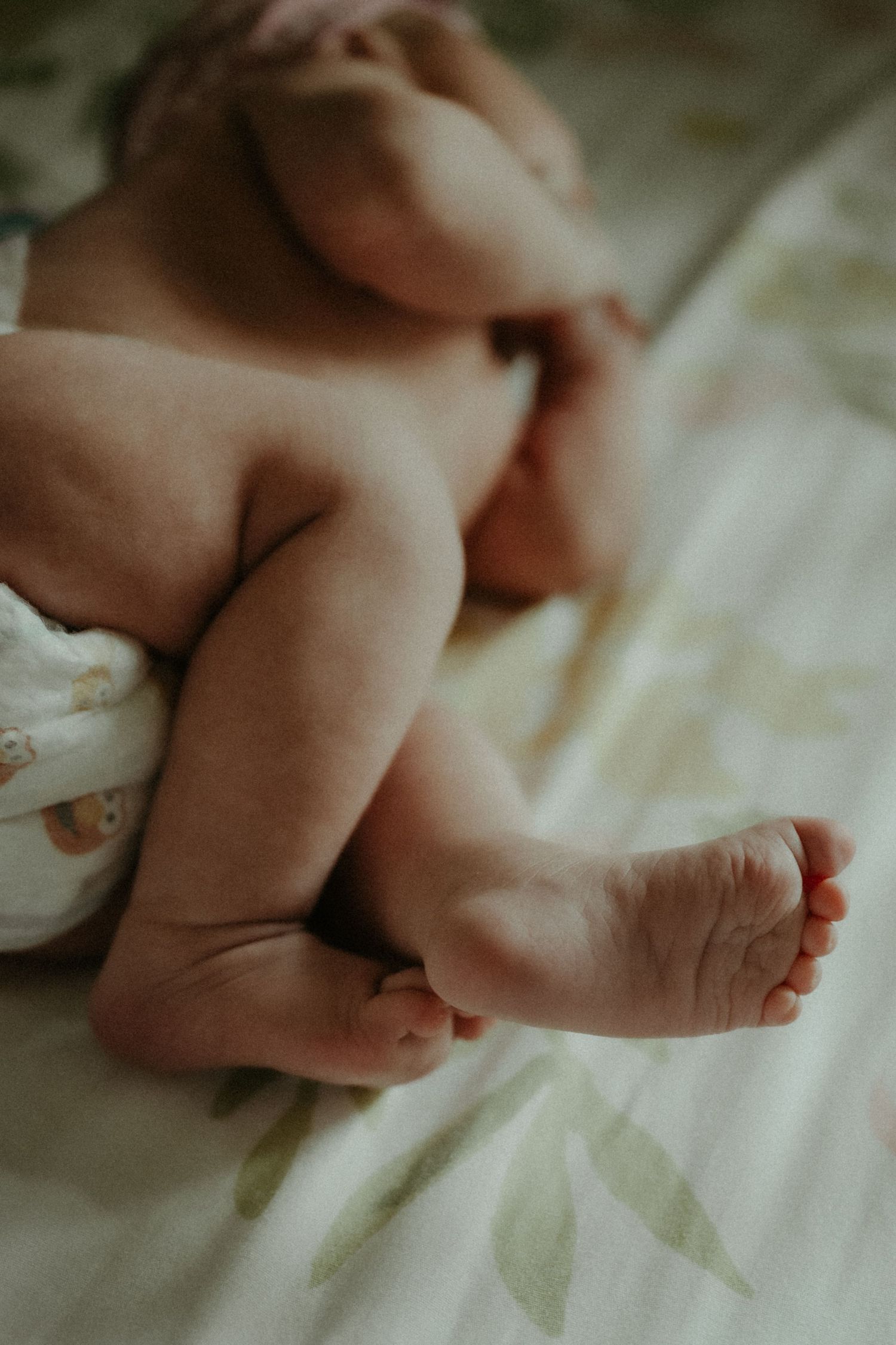 Close-up of a sleeping baby's bare feet and legs resting on soft white patterned bedding. Pittsburgh / Westmoreland Photographer