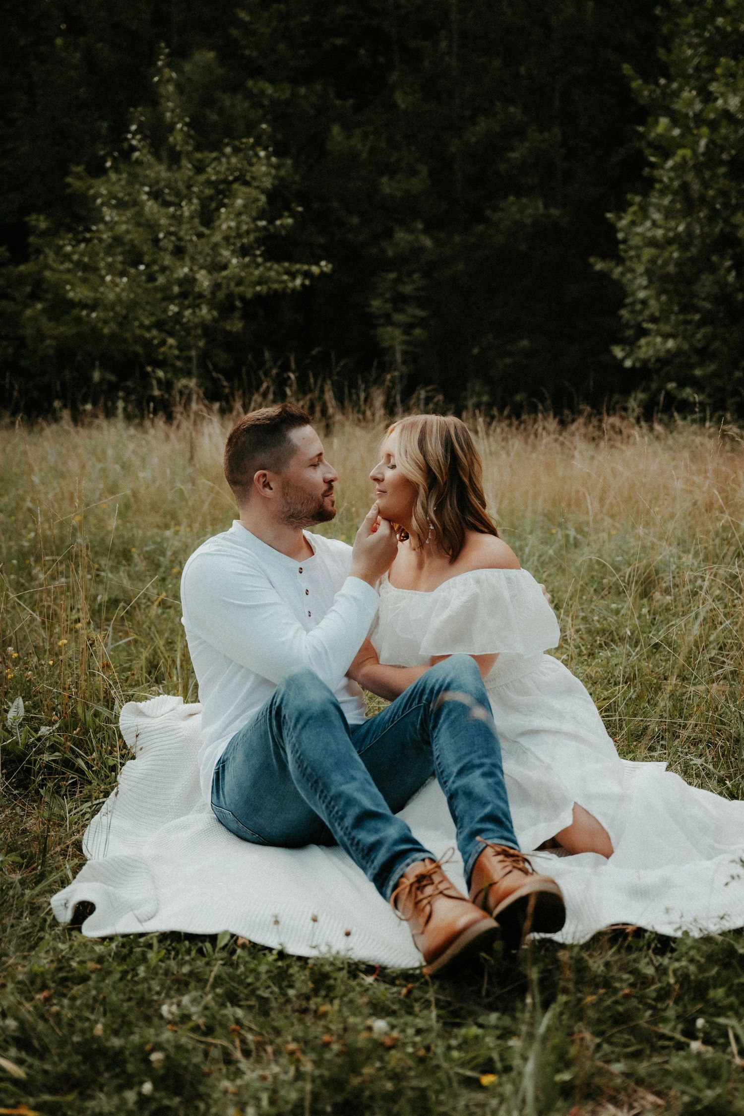 A romantic couple sits on a white blanket in a rustic field surrounded by tall grass and trees. Pittsburgh Wedding Photographer
