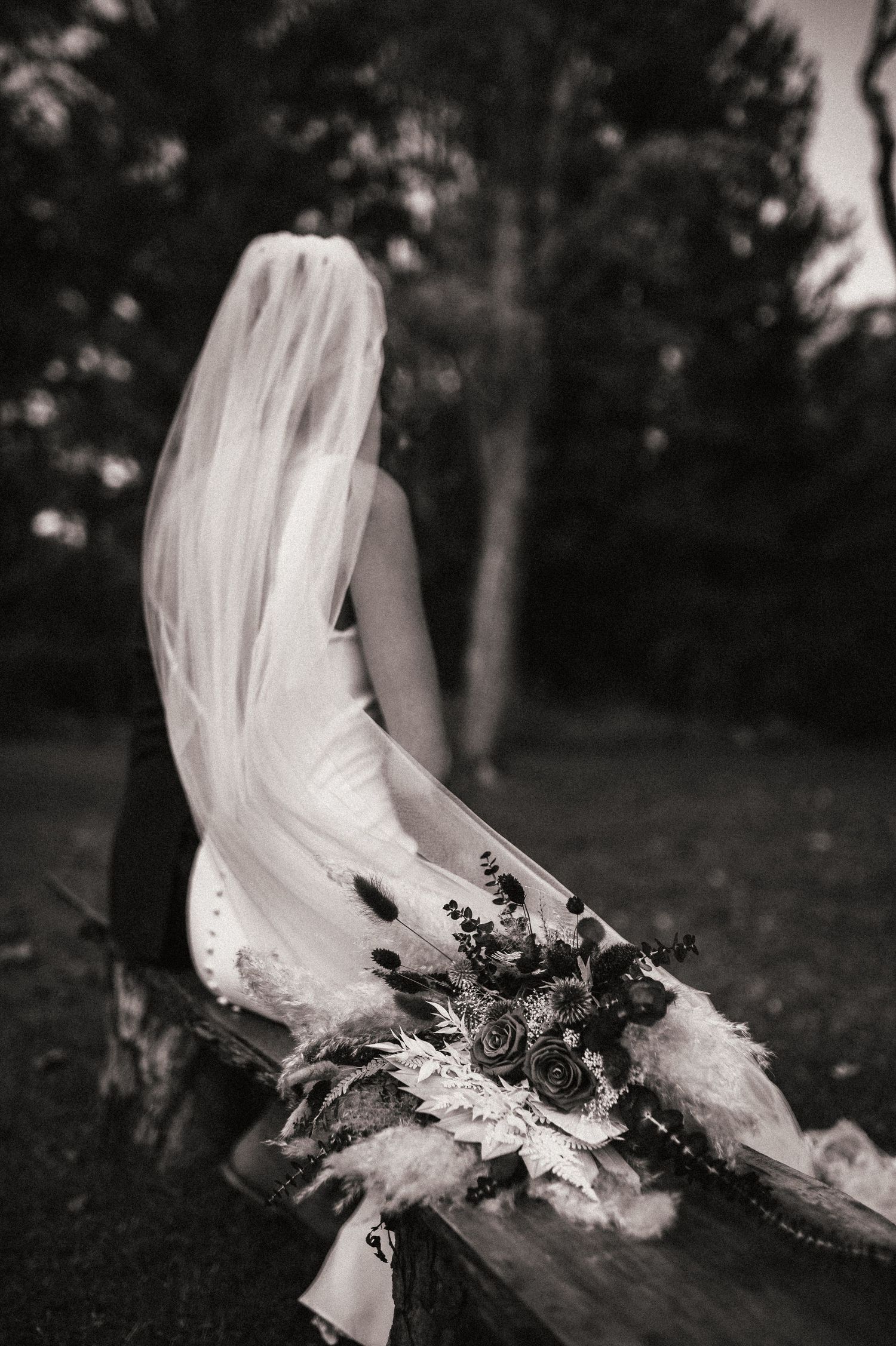 A bride in white dress poses dramatically with flowing veil and bouquet in a garden setting. Pittsburgh Wedding Photographer
