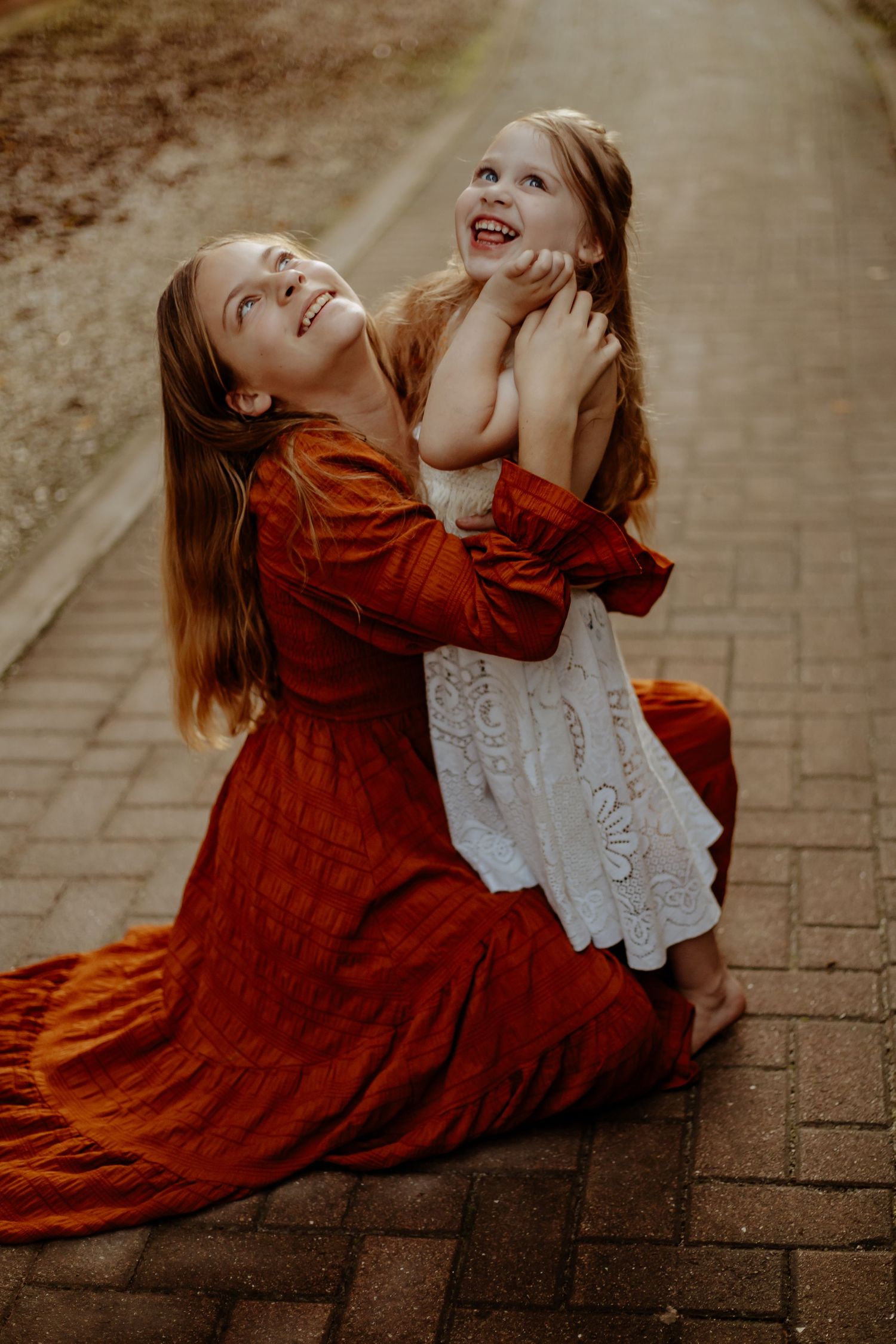 A series of artistic photos showing a person in a rust-colored dress laying on brick pavement in dramatic poses.