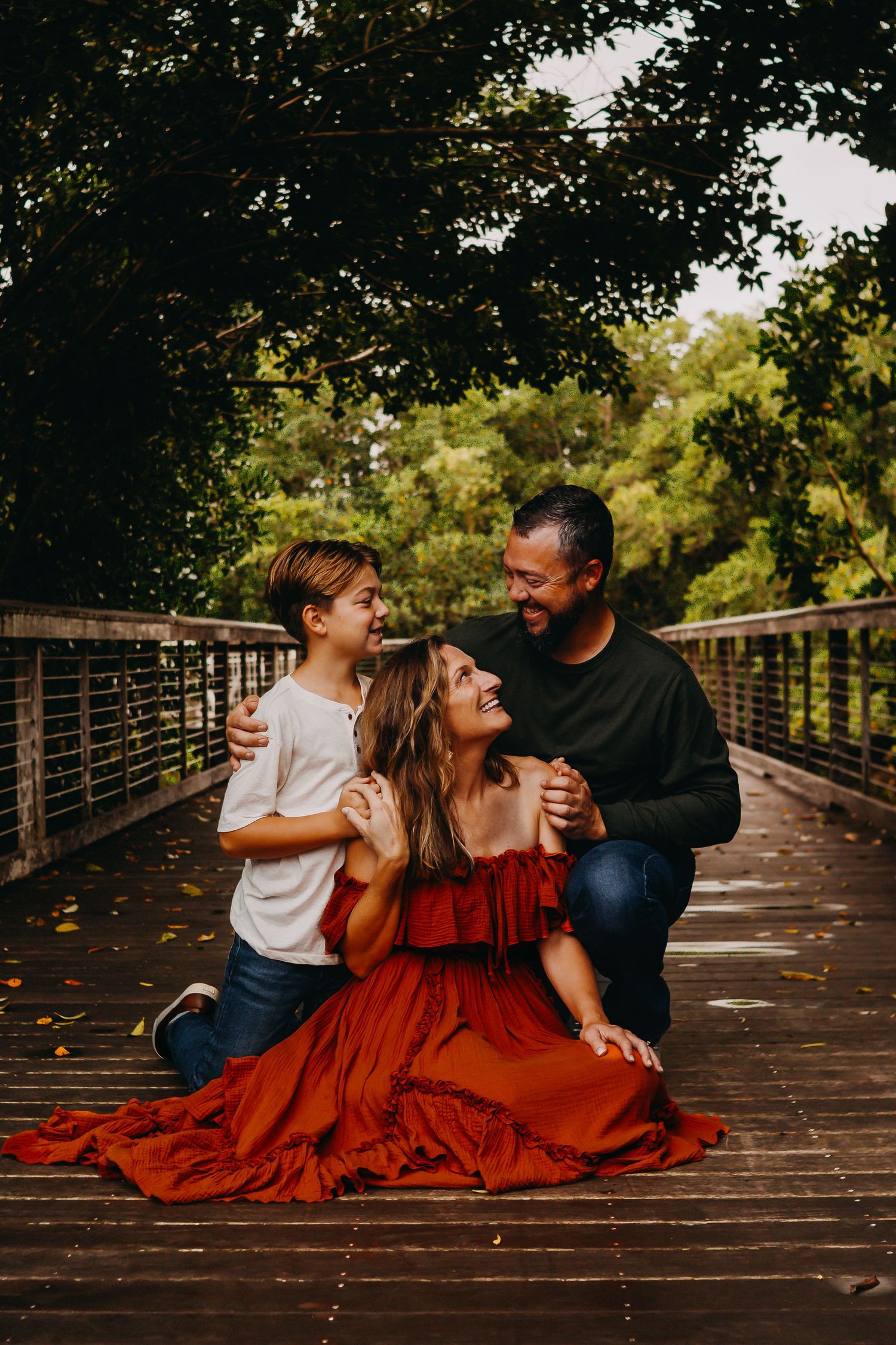 A family shares a joyful moment together on a wooden bridge surrounded by autumn trees and fallen leaves.