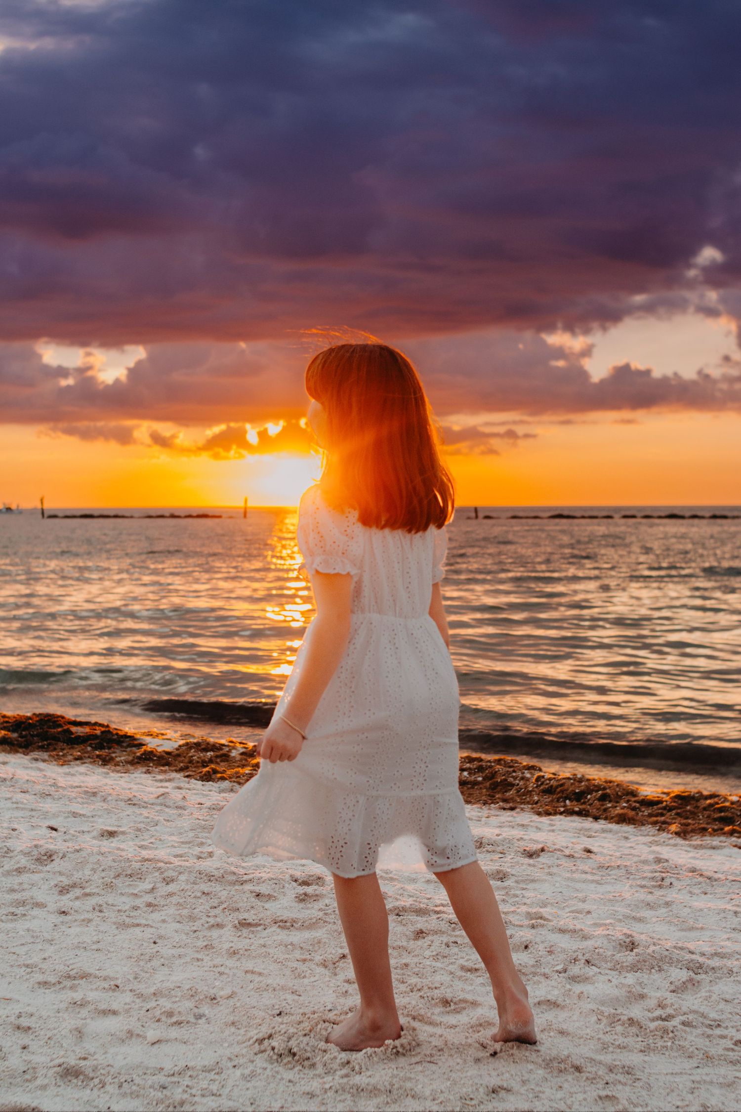 A series of sunset beach photos showing a person in white clothing watching the golden sun sink into the ocean horizon.