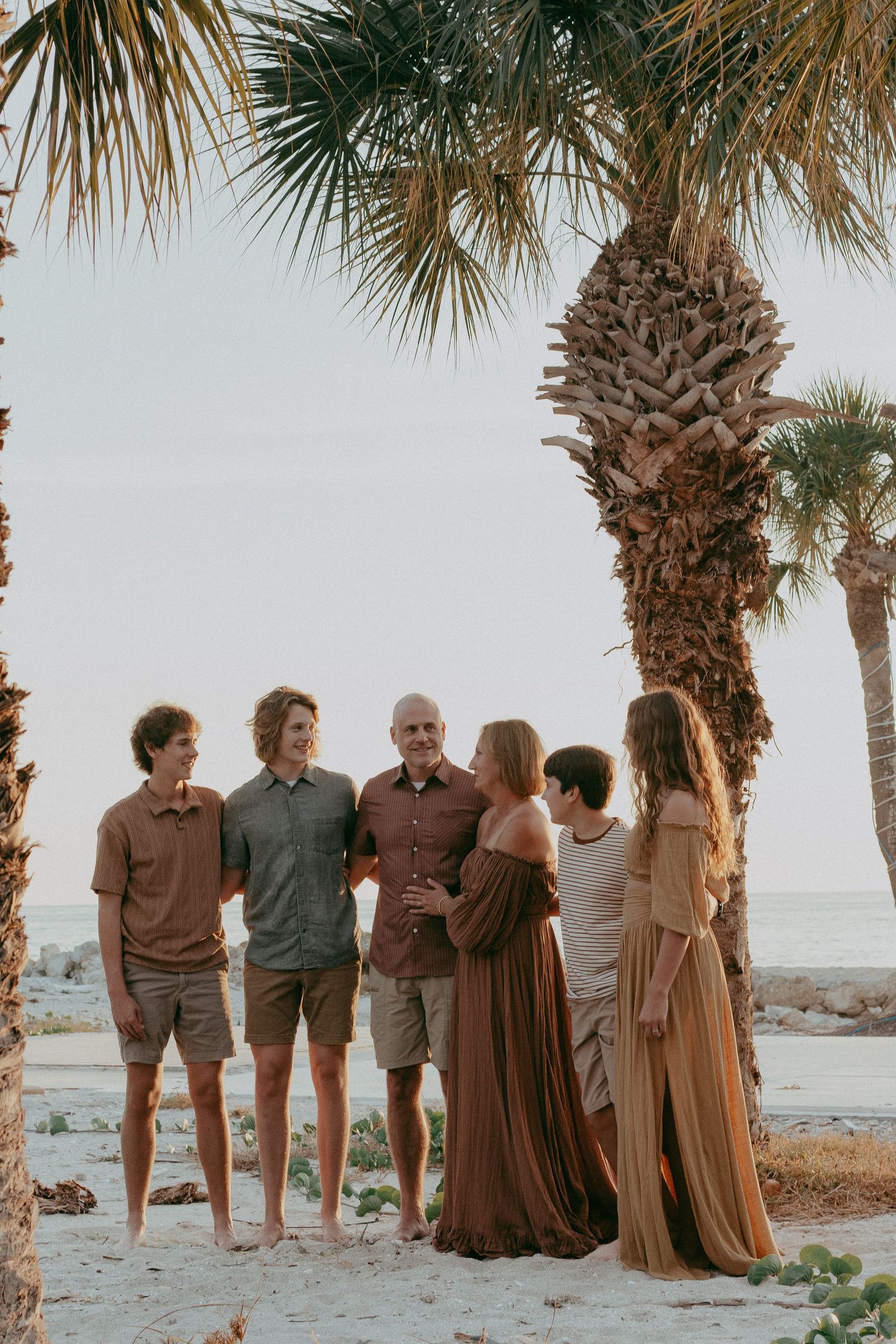 A group stands together on a beach at sunset with palm trees and ocean in the background.