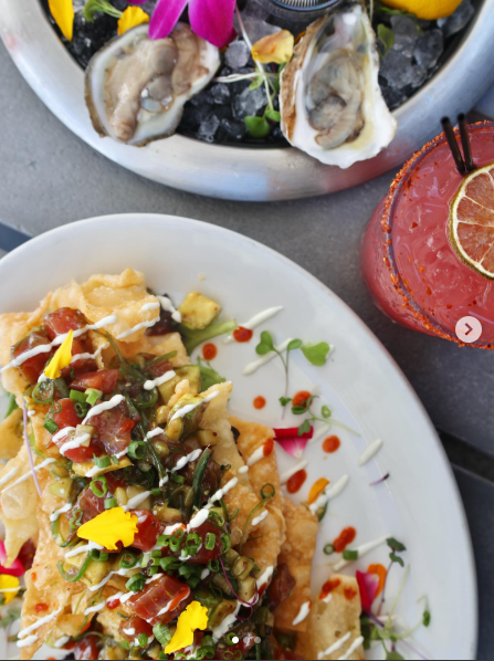 Fresh seafood tacos garnished with colorful toppings and sauce drizzles on white plates arranged in a row.