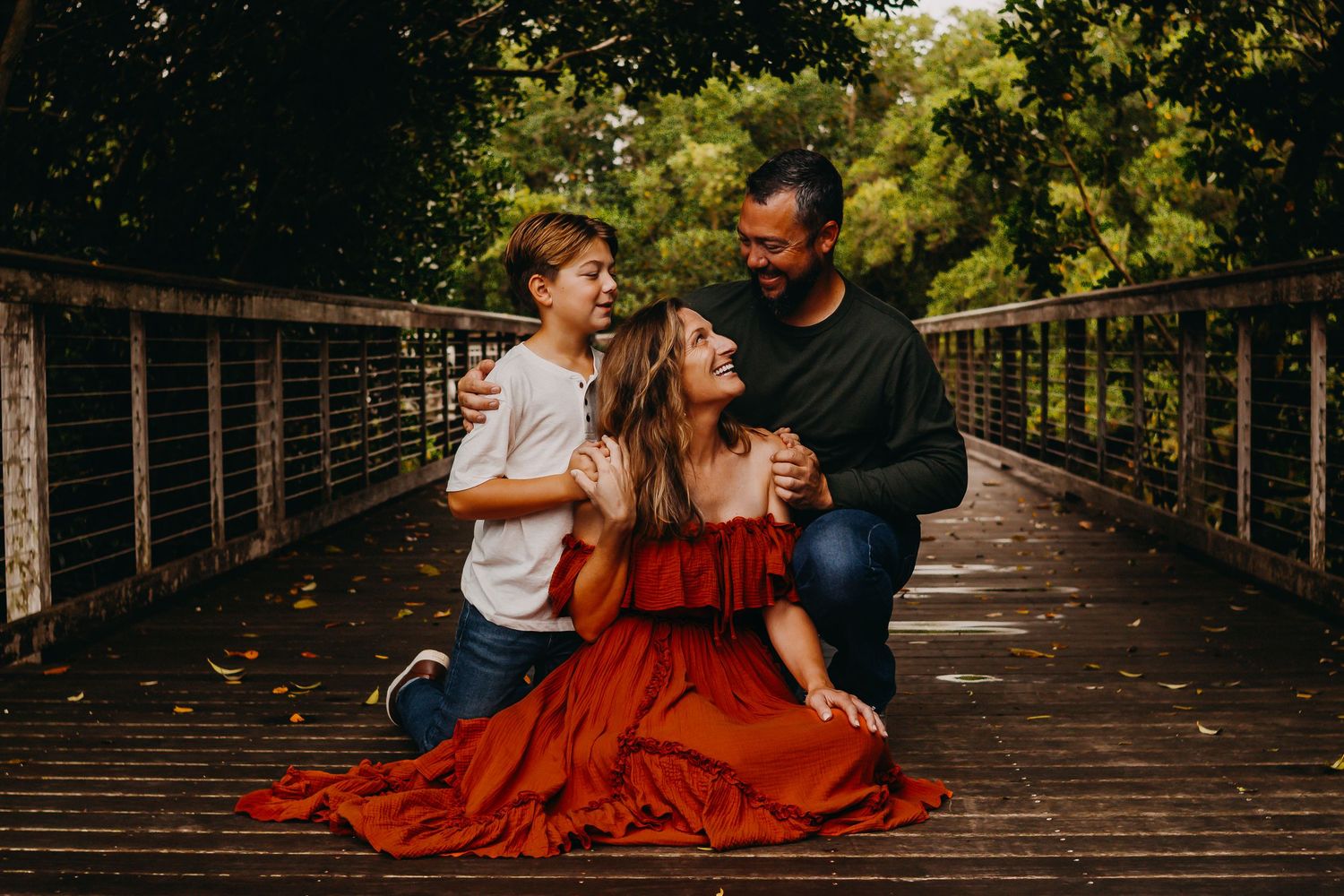 A couple in autumn attire shares tender moments on a rustic wooden bridge surrounded by lush greenery.