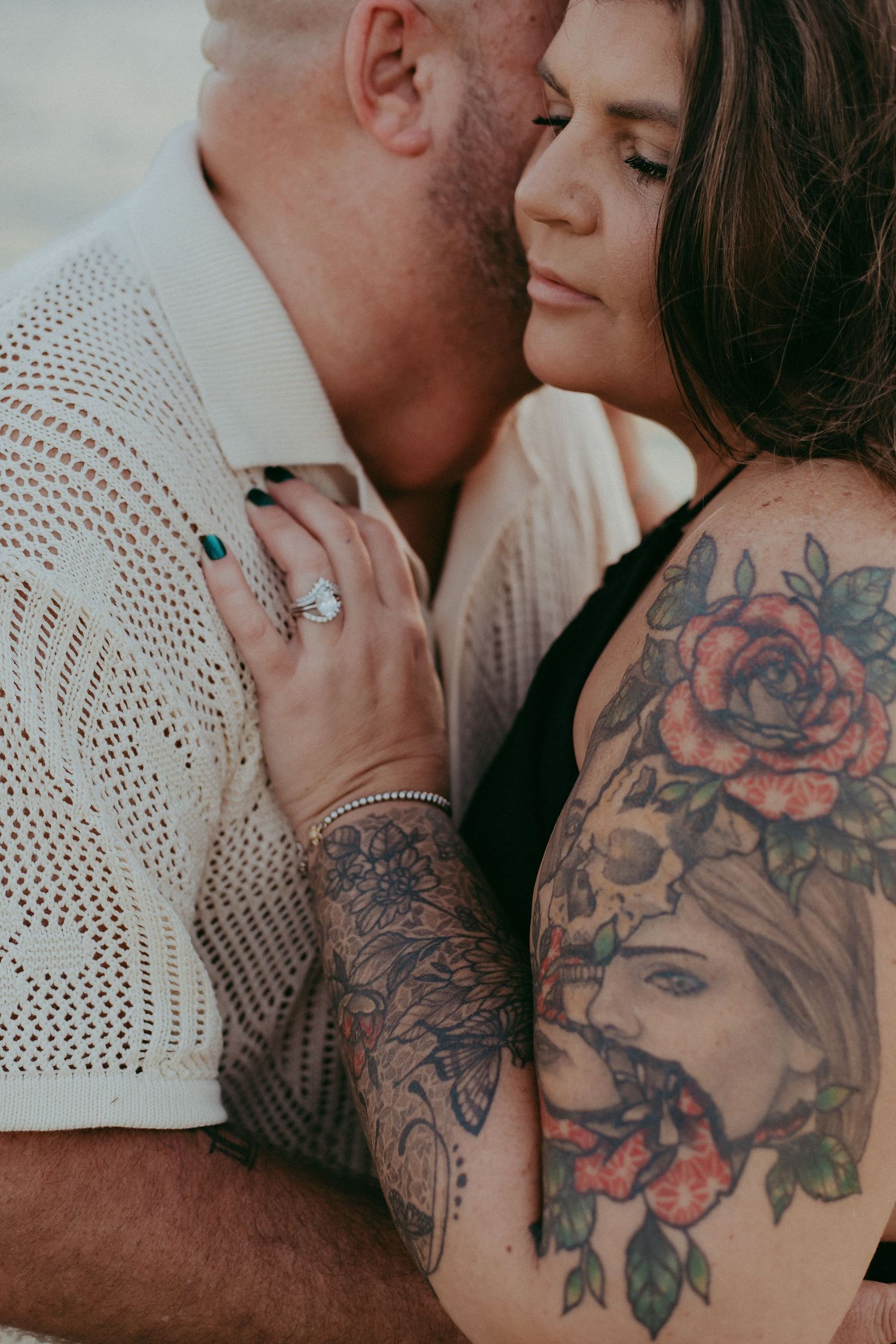 Close-up photos of a couple embracing, showing detailed floral tattoo artwork on skin against white knit fabric.