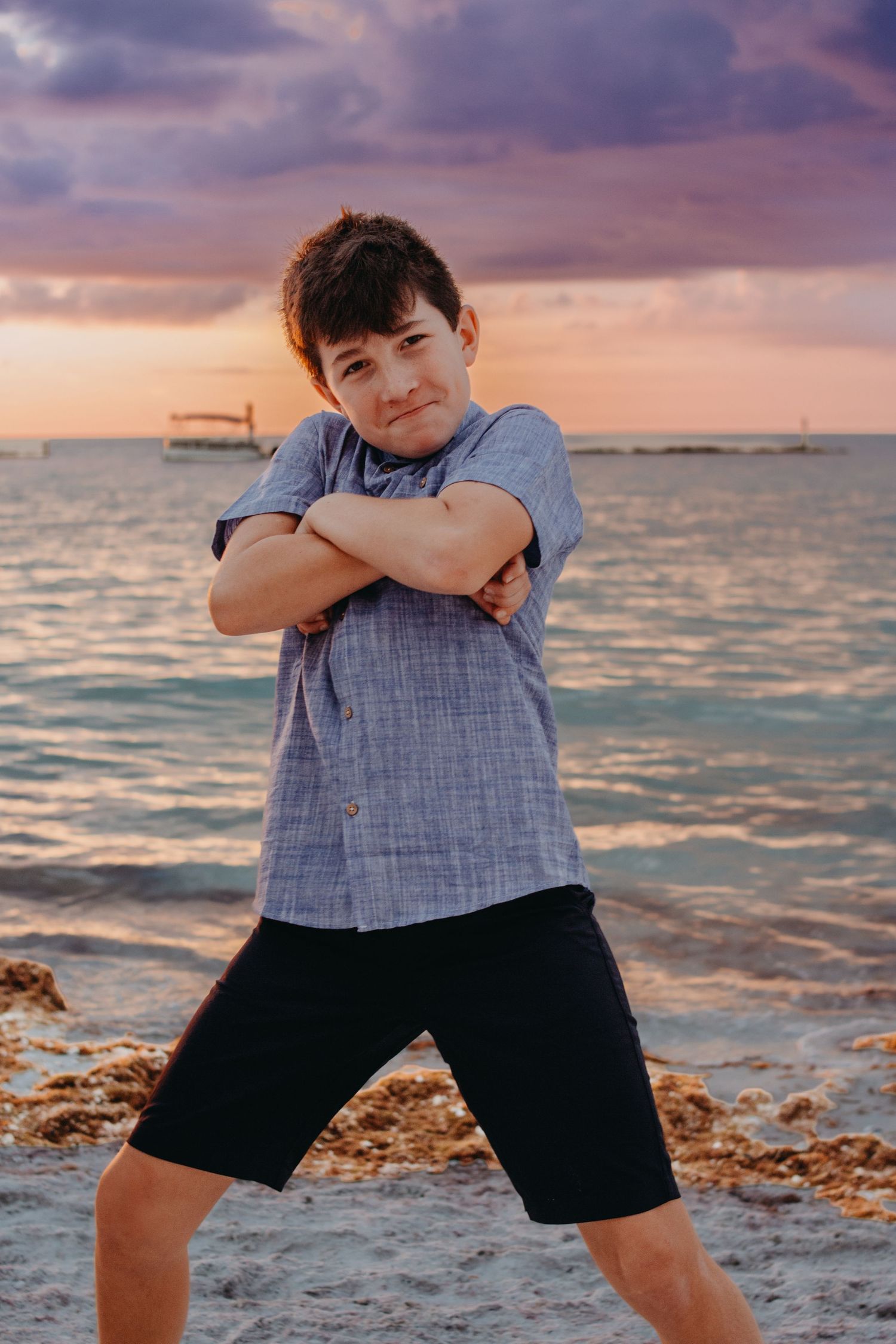 A series of photos showing someone in a blue shirt and dark shorts posing playfully on a beach at sunset.