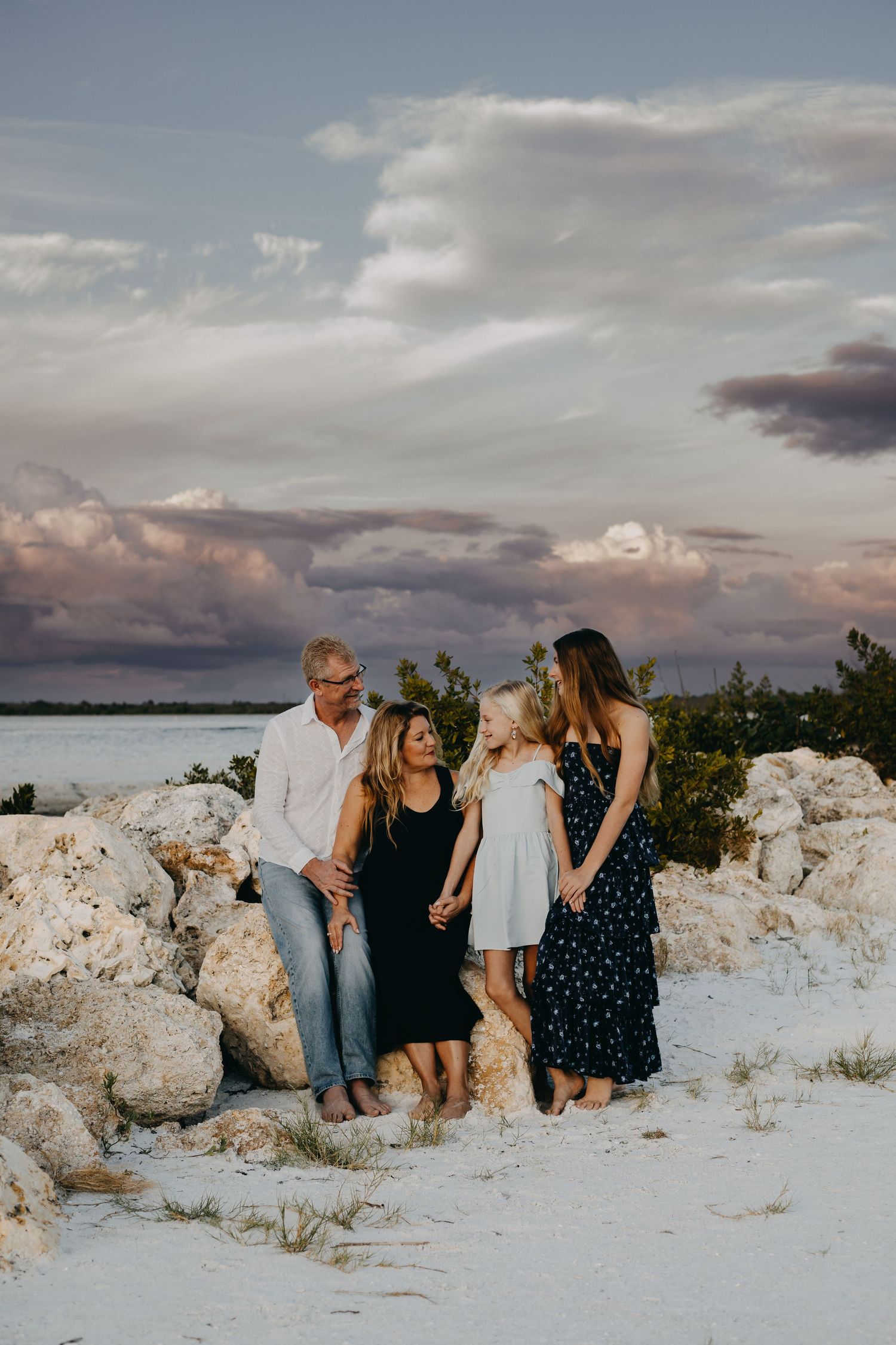 A group sits together on white limestone rocks at sunset against a cloudy sky and coastal backdrop.