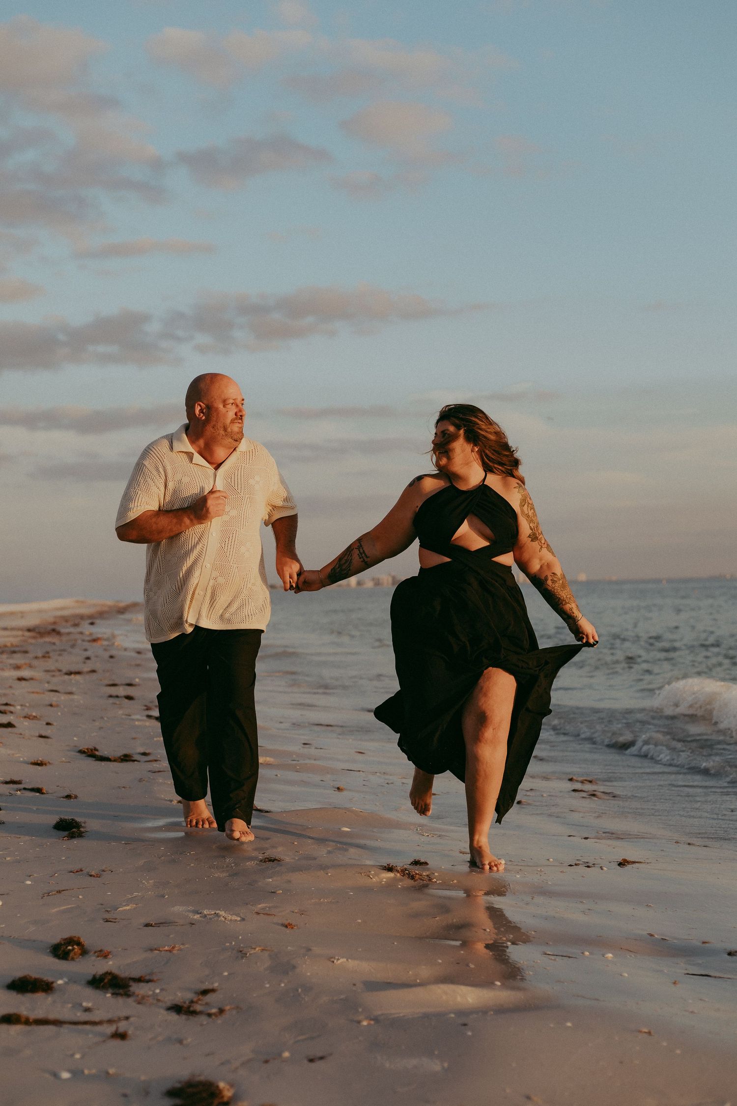 A couple dances joyfully together on a beach at sunset, creating a romantic and playful scene by the ocean.
