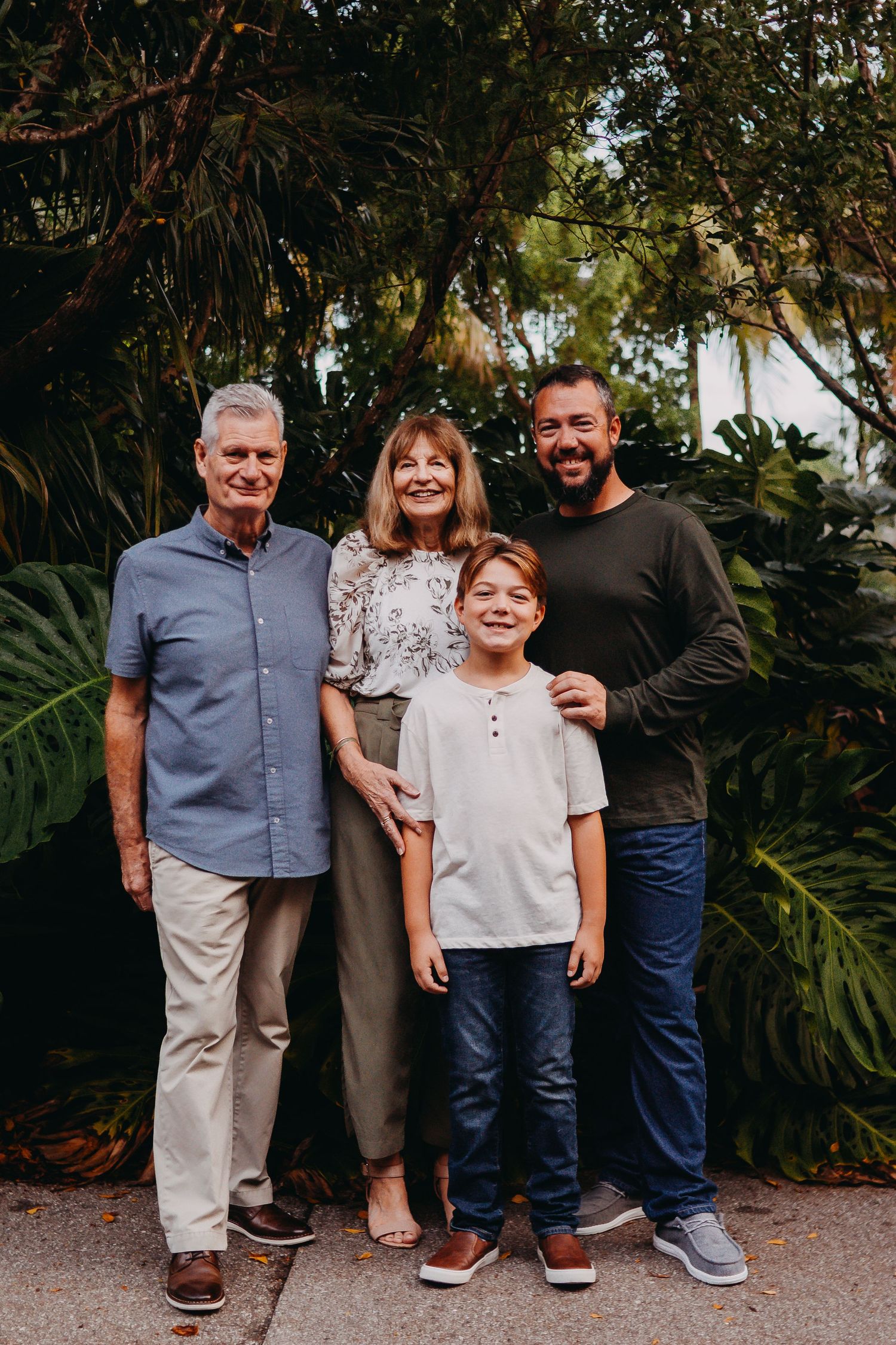 A group of people stand together outdoors against a lush tropical garden backdrop in natural lighting.