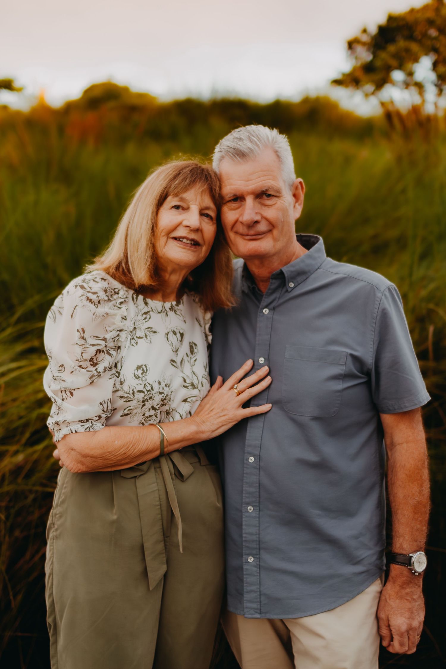 A senior couple embraces during a warm sunset photoshoot in a natural outdoor setting.