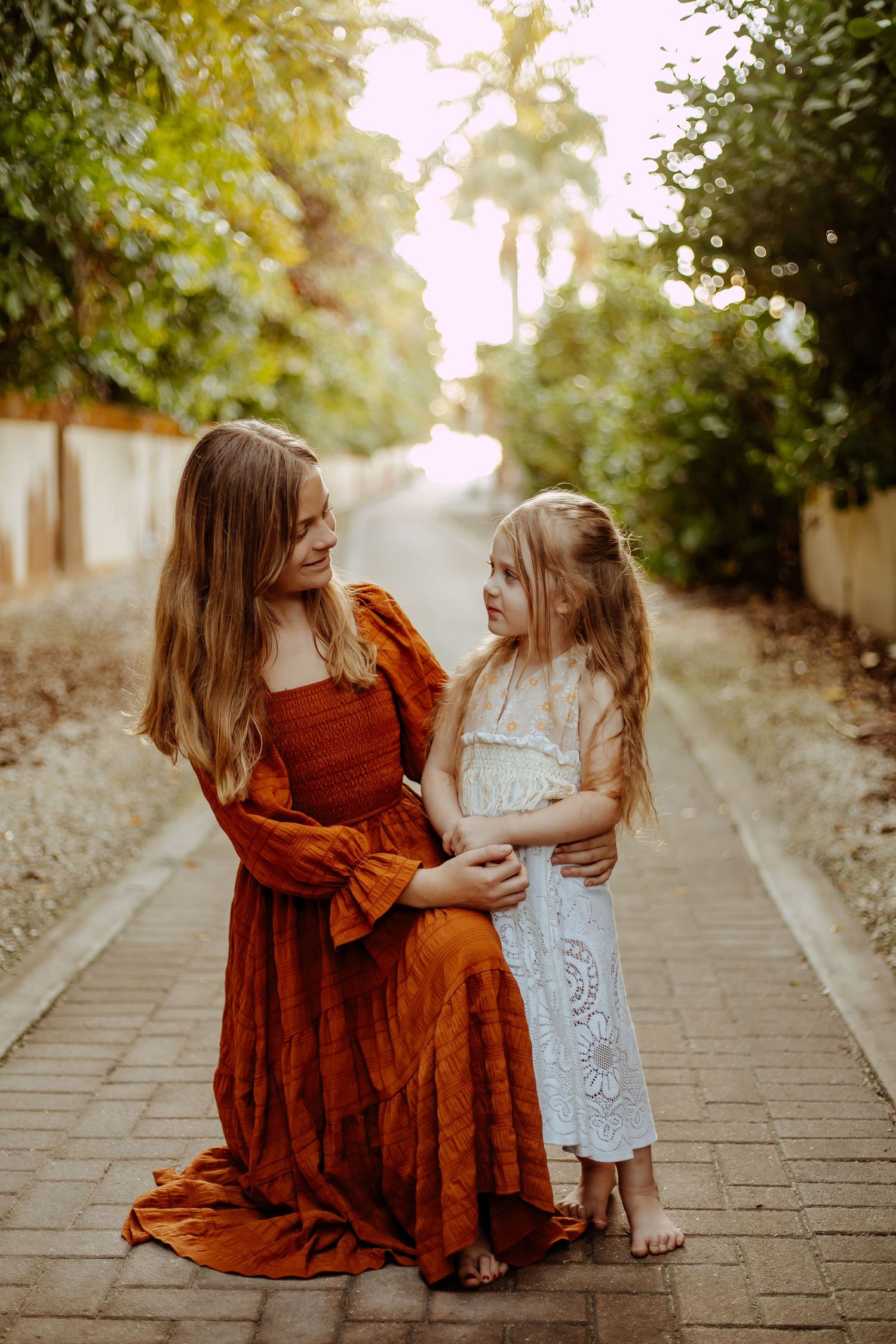 Two people in casual dresses share a tender moment while sitting on stone steps during golden hour.
