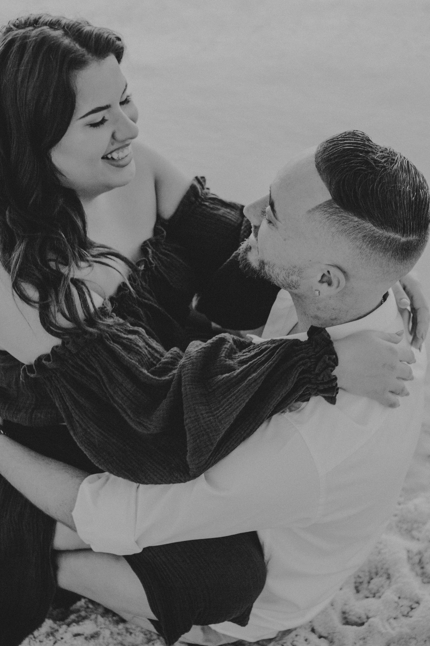 Black and white romantic photo series showing a couple embracing and laughing together in the snow.