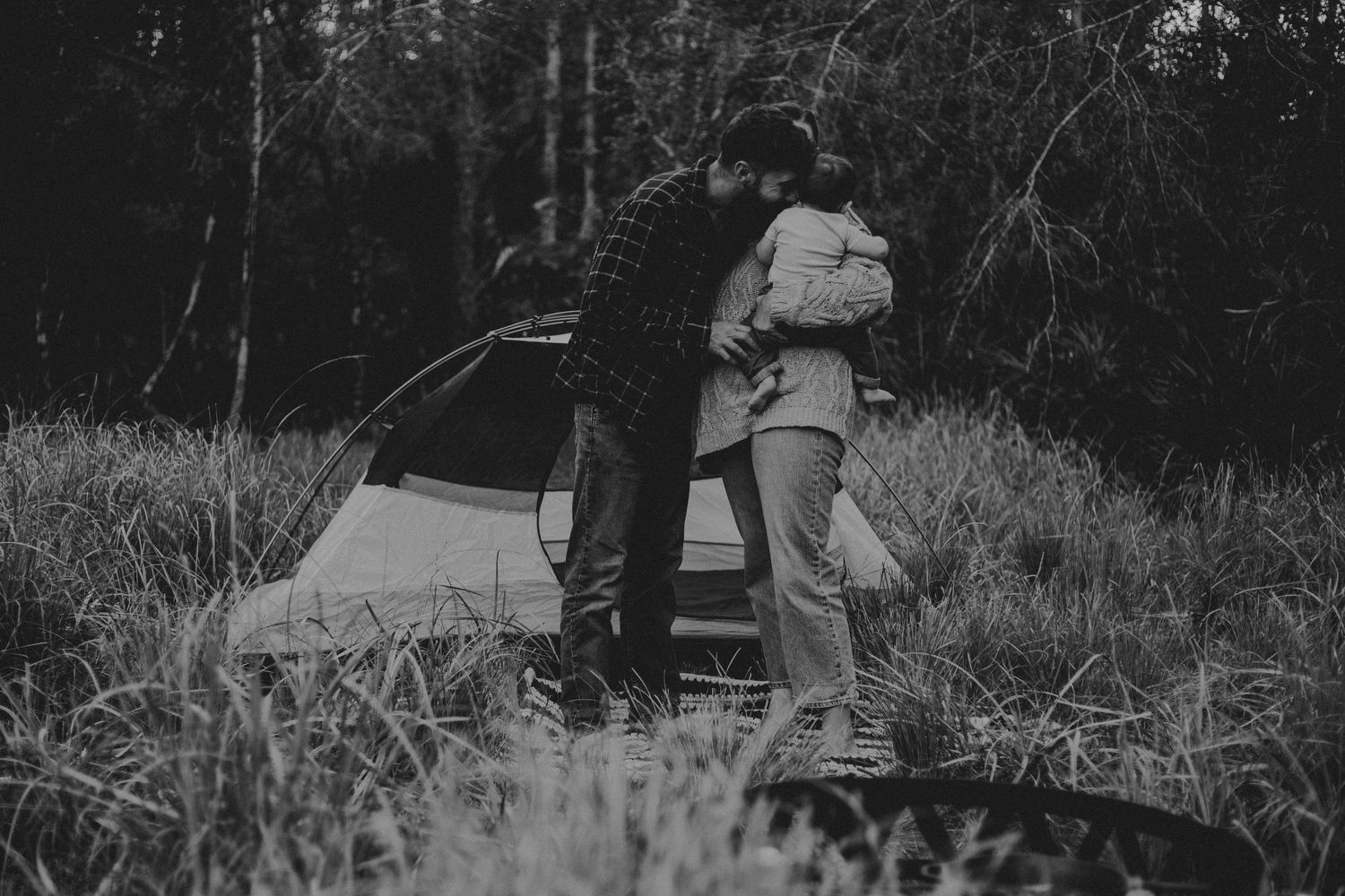 A couple sits together on a blanket during a romantic black and white outdoor picnic in a wooded area.