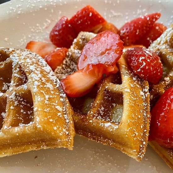 Golden waffle pieces dusted with powdered sugar and topped with fresh sliced strawberries on a white plate.