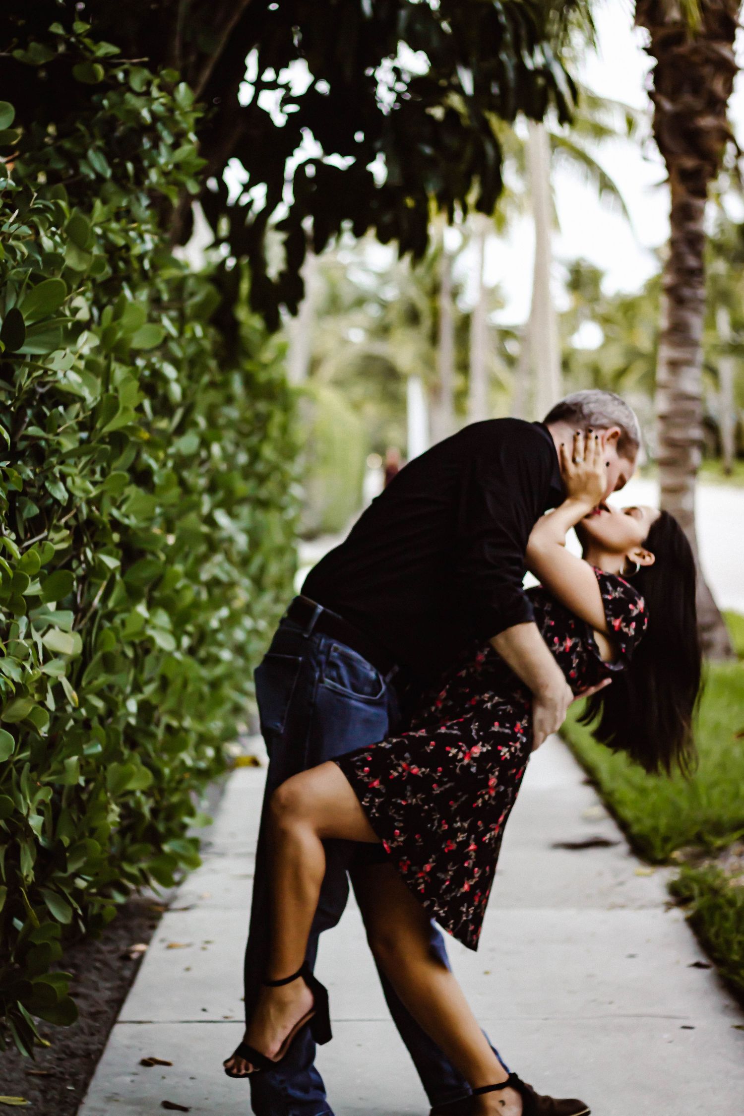 A couple dancing and dipping together on a palm tree-lined pathway.