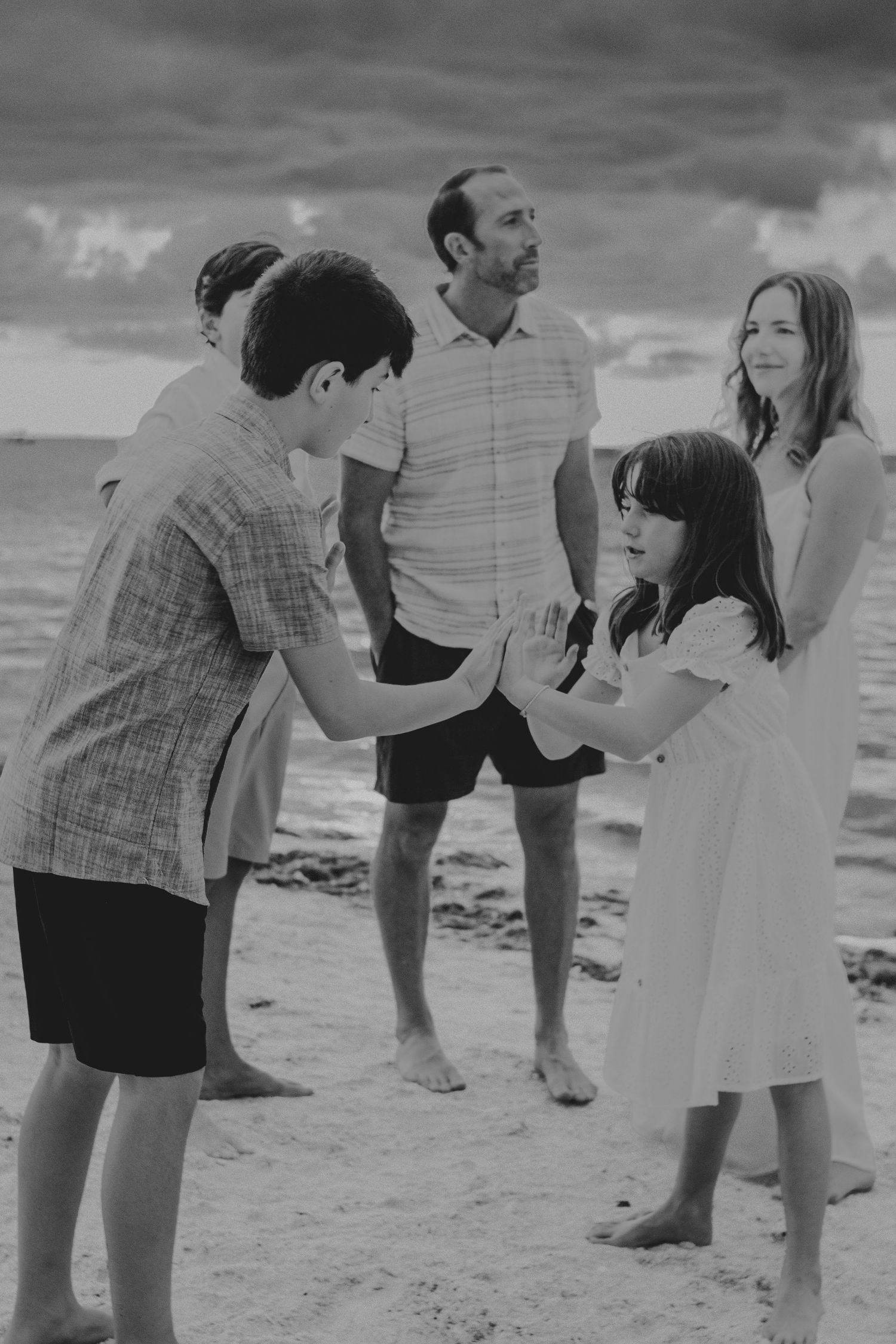 A sequence of black and white photos showing people walking and interacting on a beach in casual summer attire.