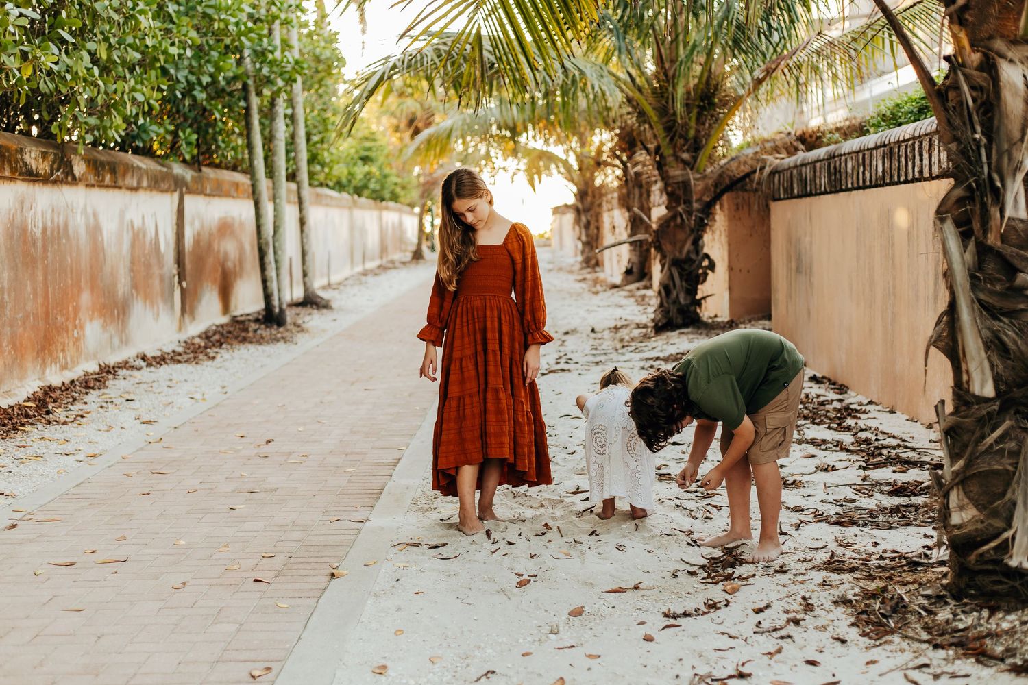 A family walks down a palm-lined path in tropical setting wearing casual vacation attire.