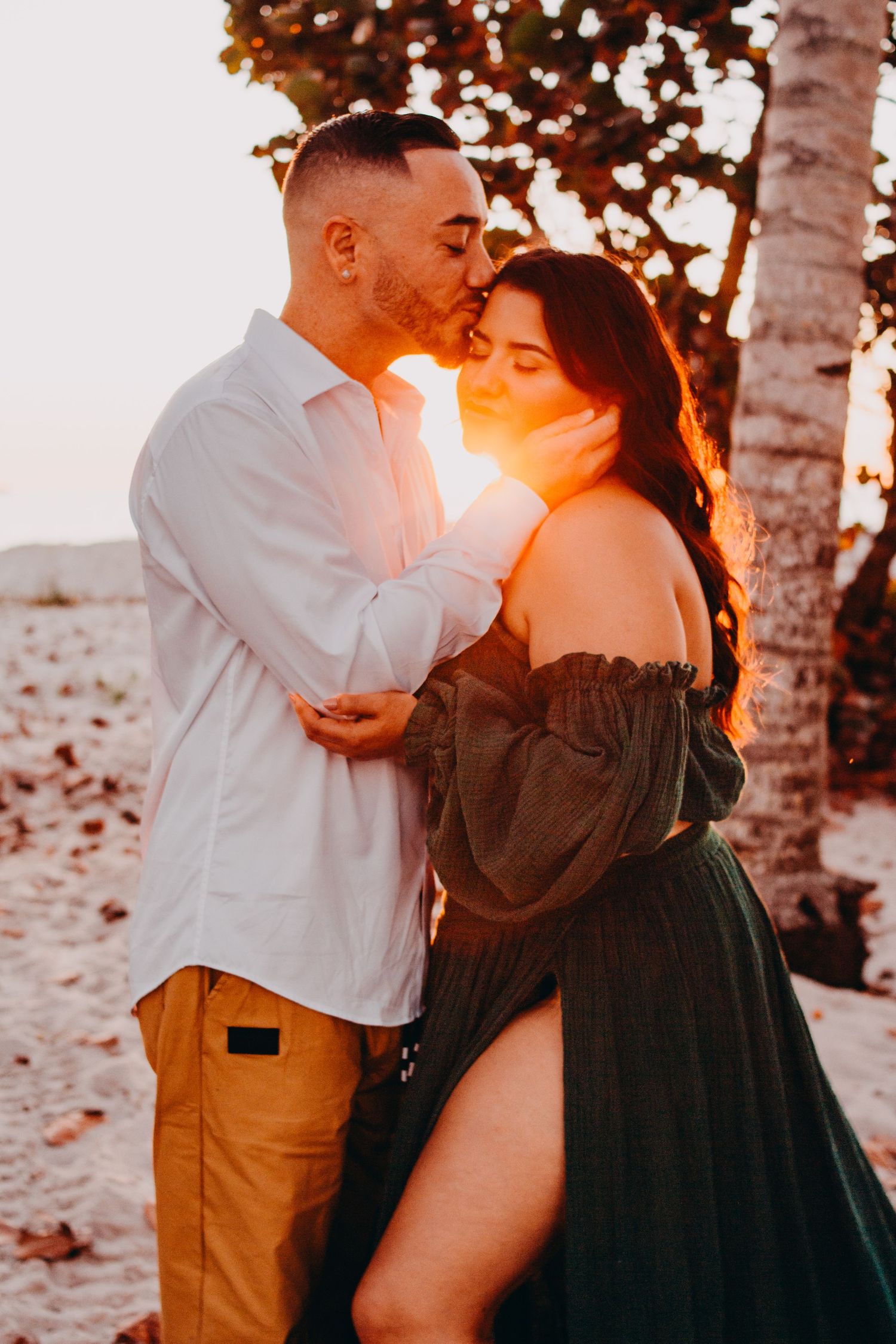 A couple embraces in romantic sunset lighting among birch trees wearing white and black attire.