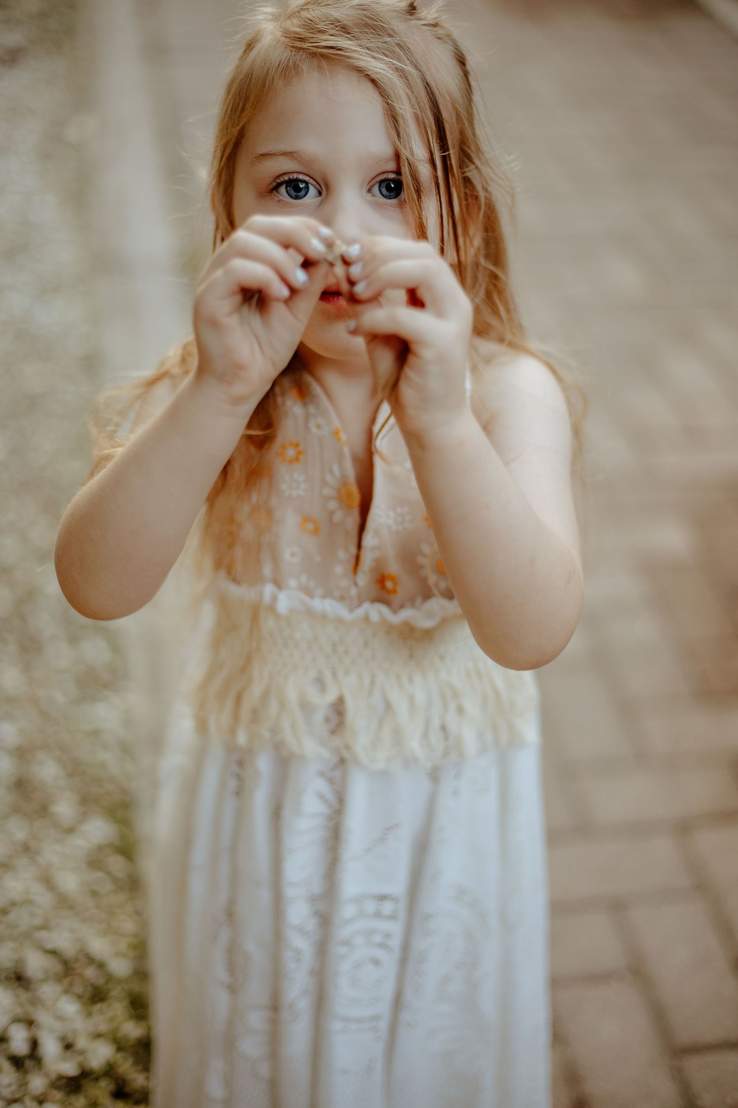 A small child in a white dress makes a playful face while standing outdoors.
