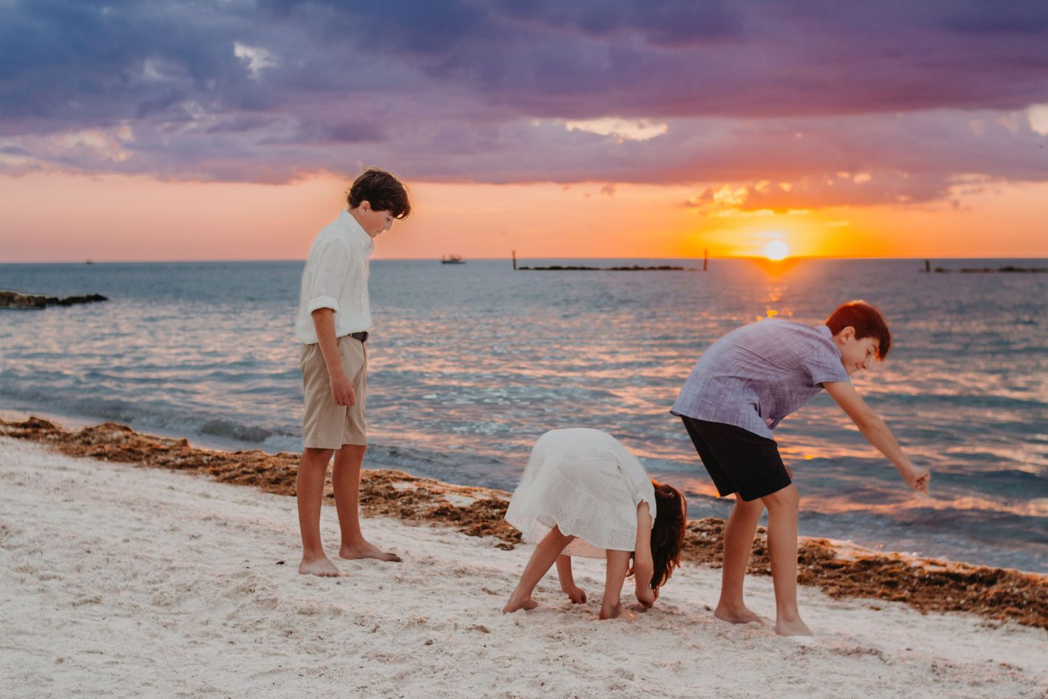 A family silhouetted against a vibrant orange sunset on a beach with gentle waves lapping at the shore.
