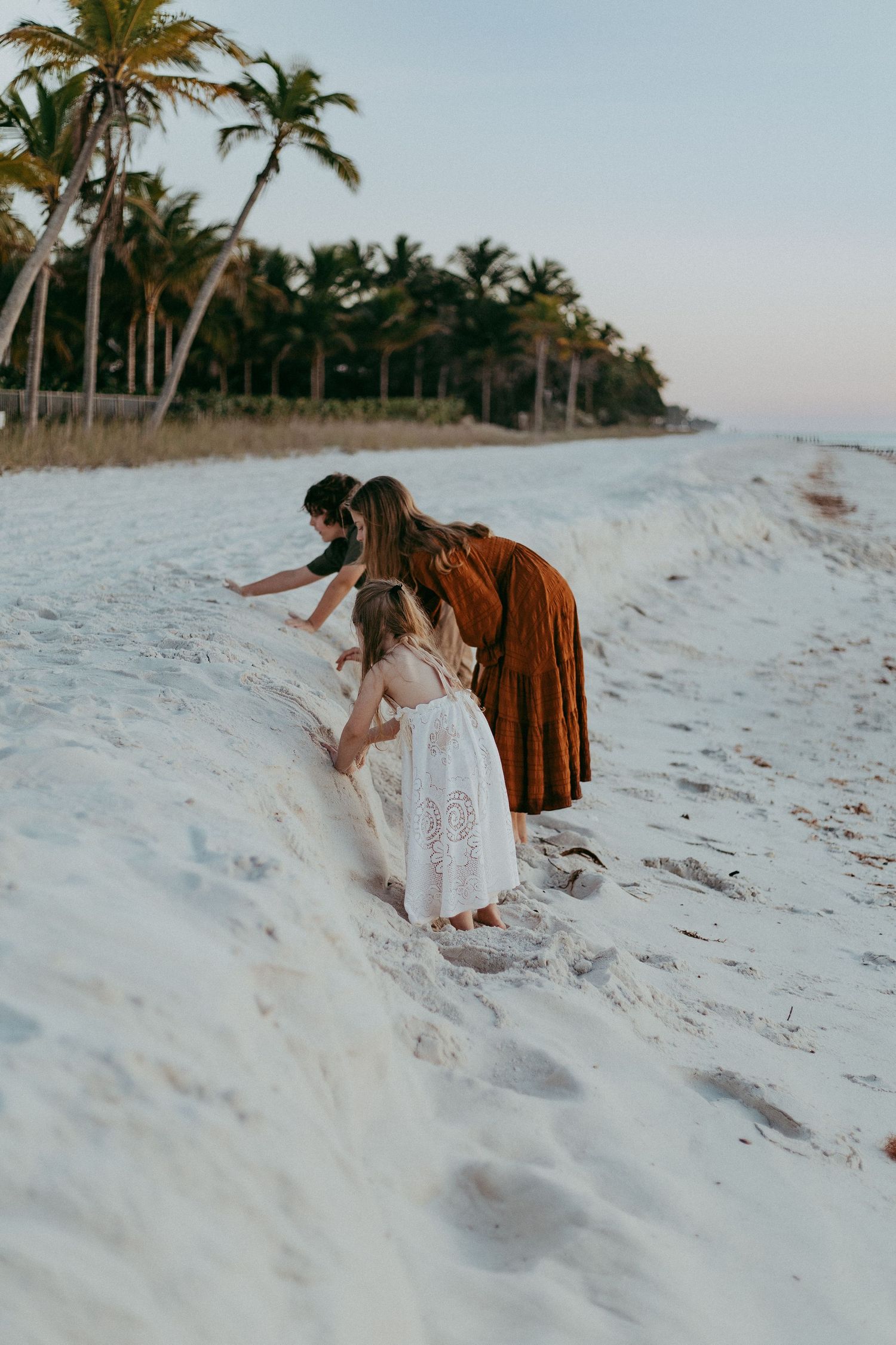 Two people in casual attire walk along a pristine white sandy beach with palm trees in the tropical background.