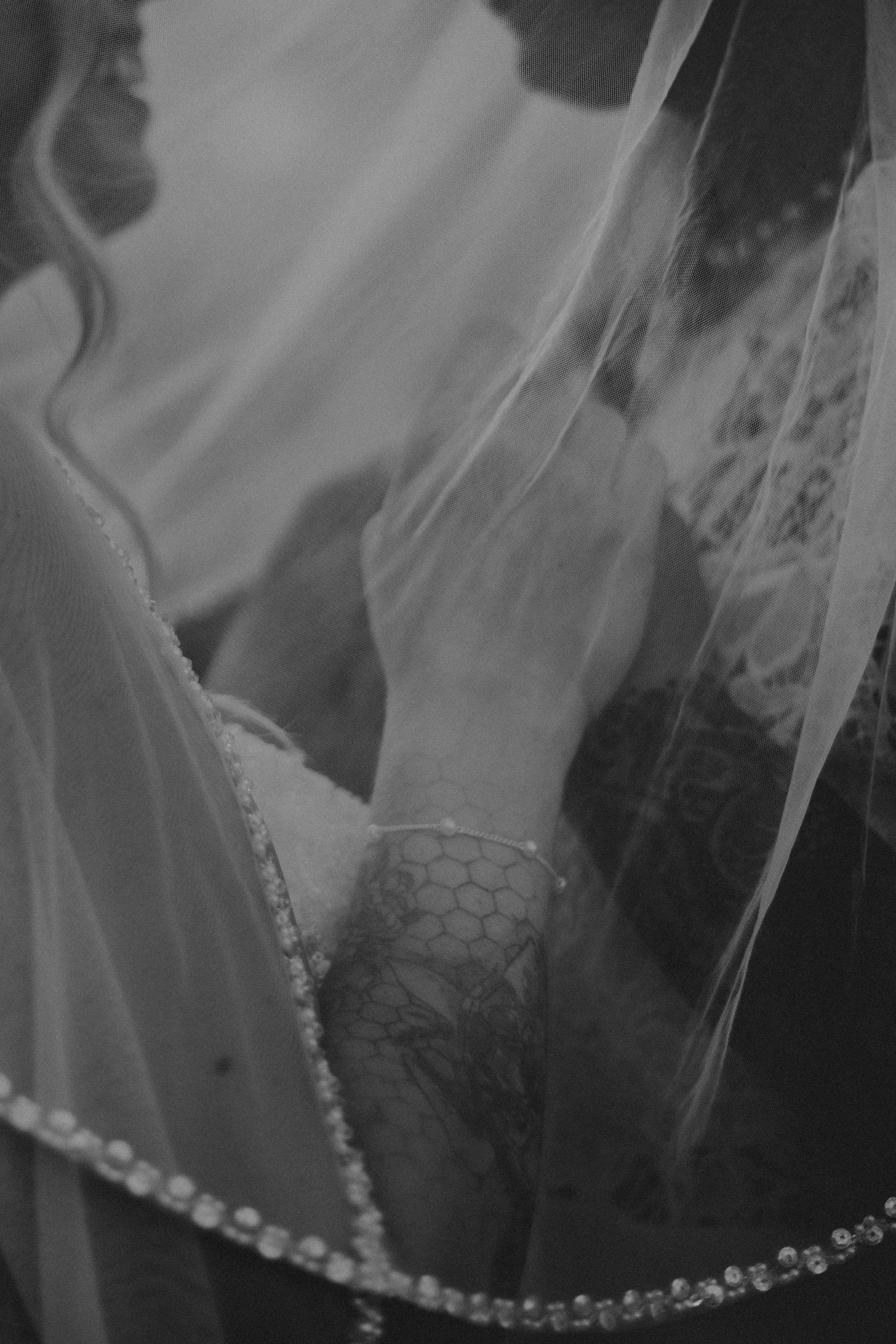 A close-up black and white photo of a delicate wedding veil with pearl embellishments.