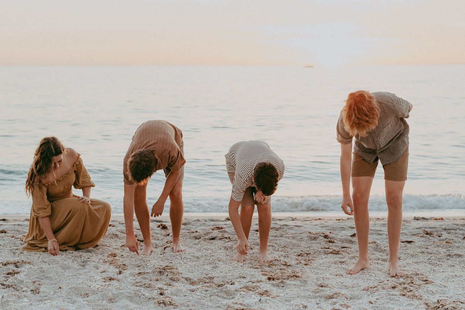 People bent over searching for shells and treasures along a sandy beach at sunset.