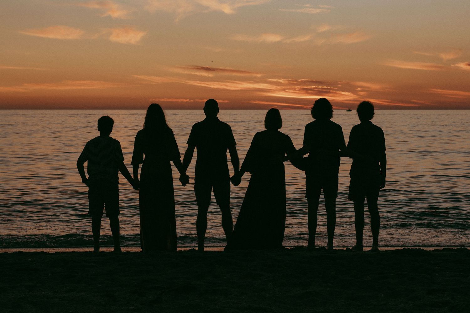 Silhouettes of people standing together against a dramatic orange sunset over the ocean.