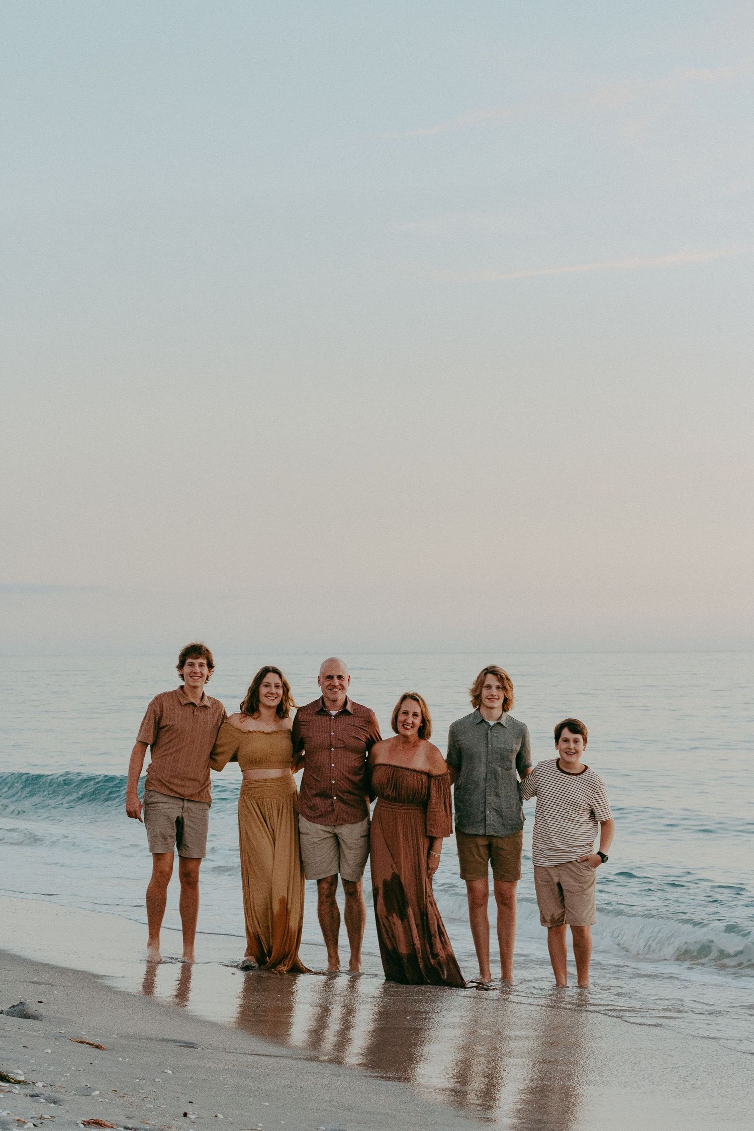 Group of people standing together on a beach at sunset with ocean waves in the background.